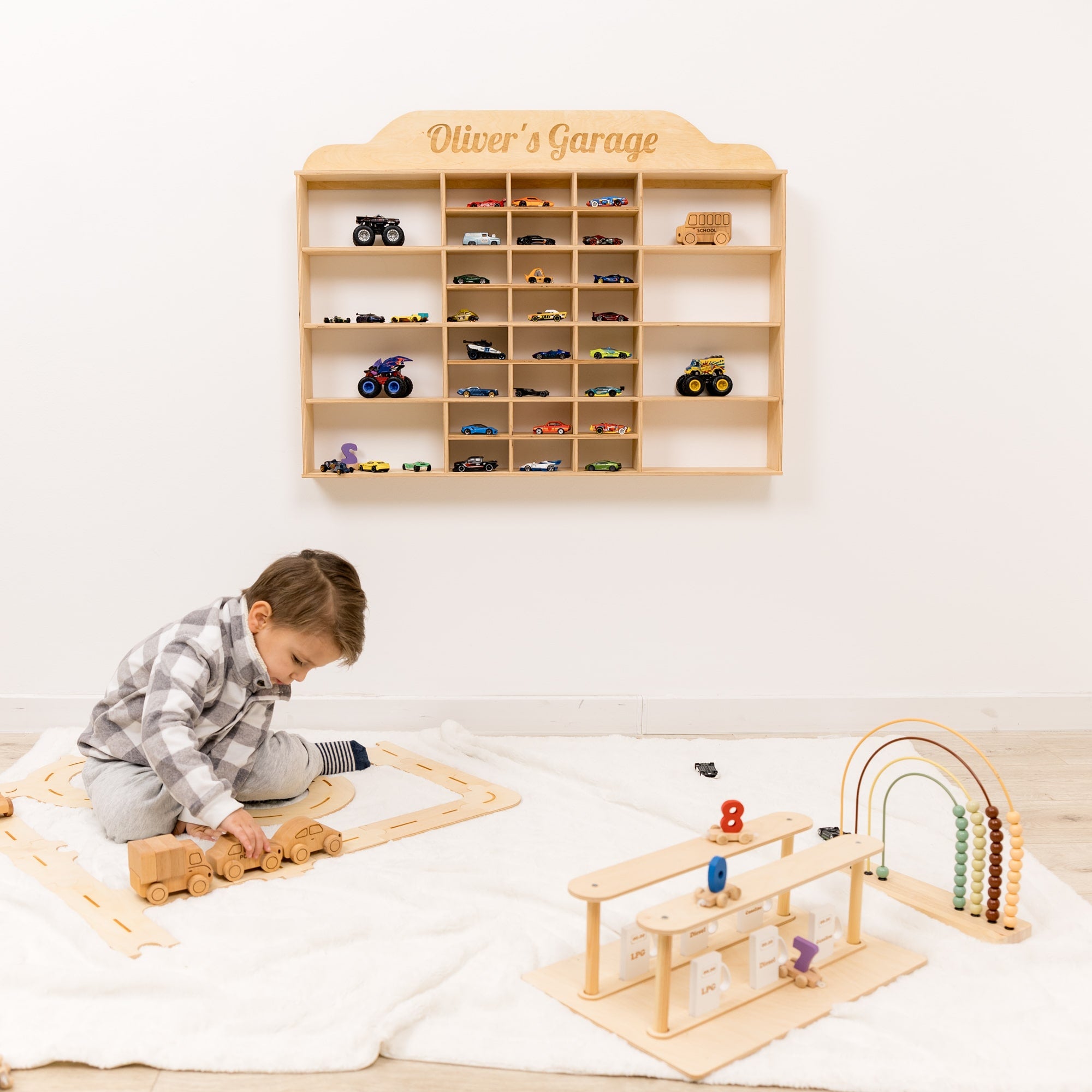 Child playing with wooden toys in front of a shelf labeled 'Oliver's Garage' filled with toy cars.