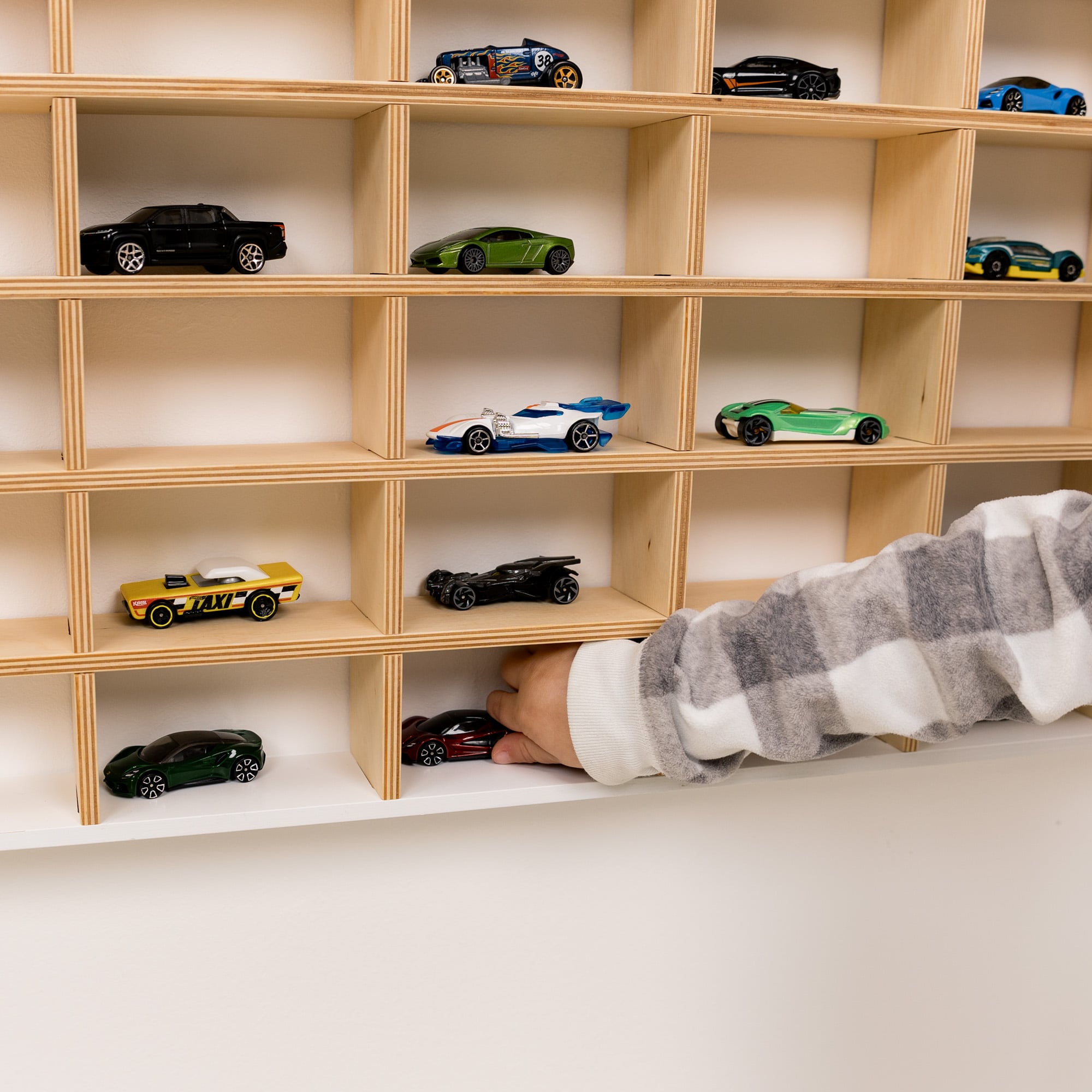 Wooden shelf with model cars and a hand reaching out to pick one up.