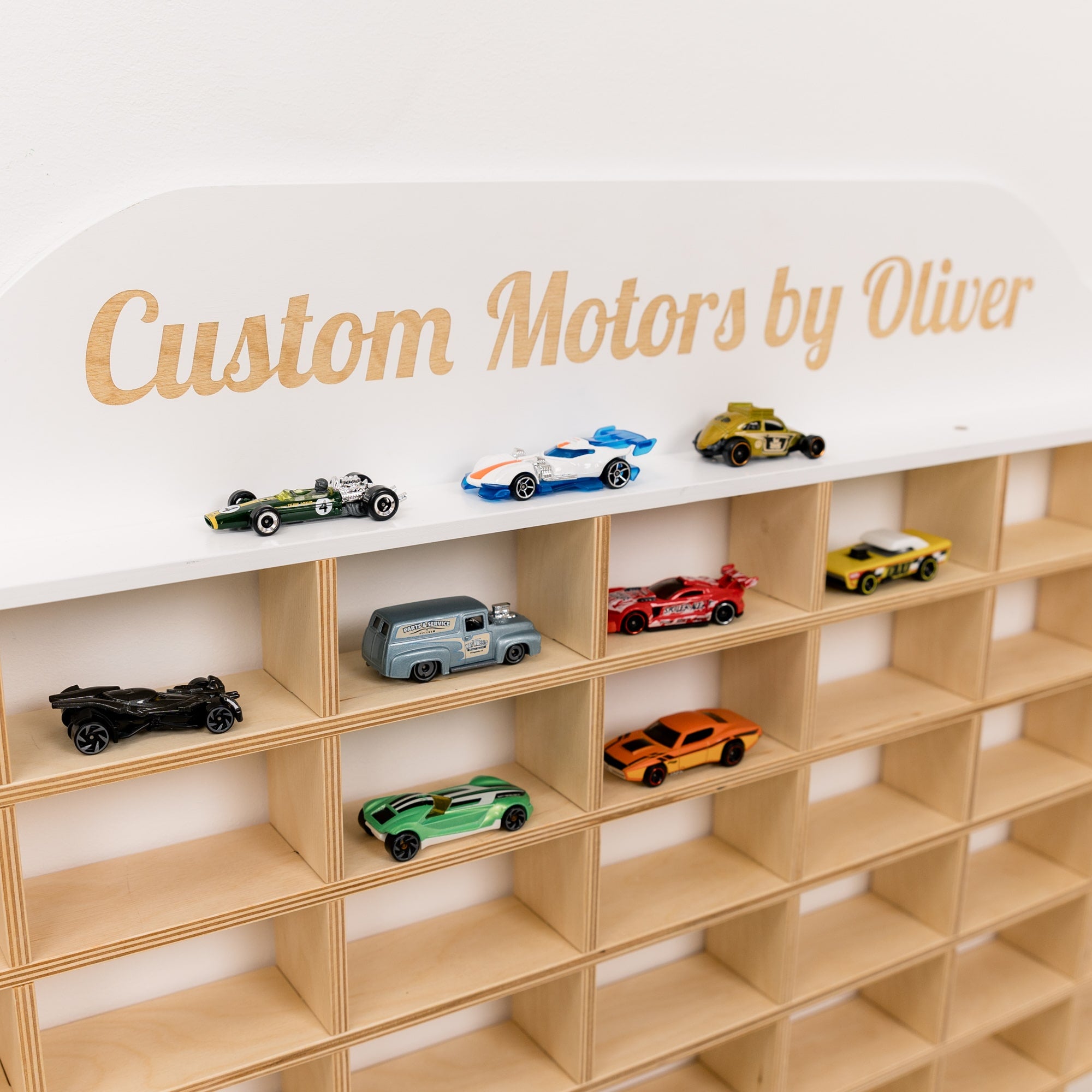 Wooden shelf with toy cars and a sign reading 'Custom Motors by Oliver' on a white background.