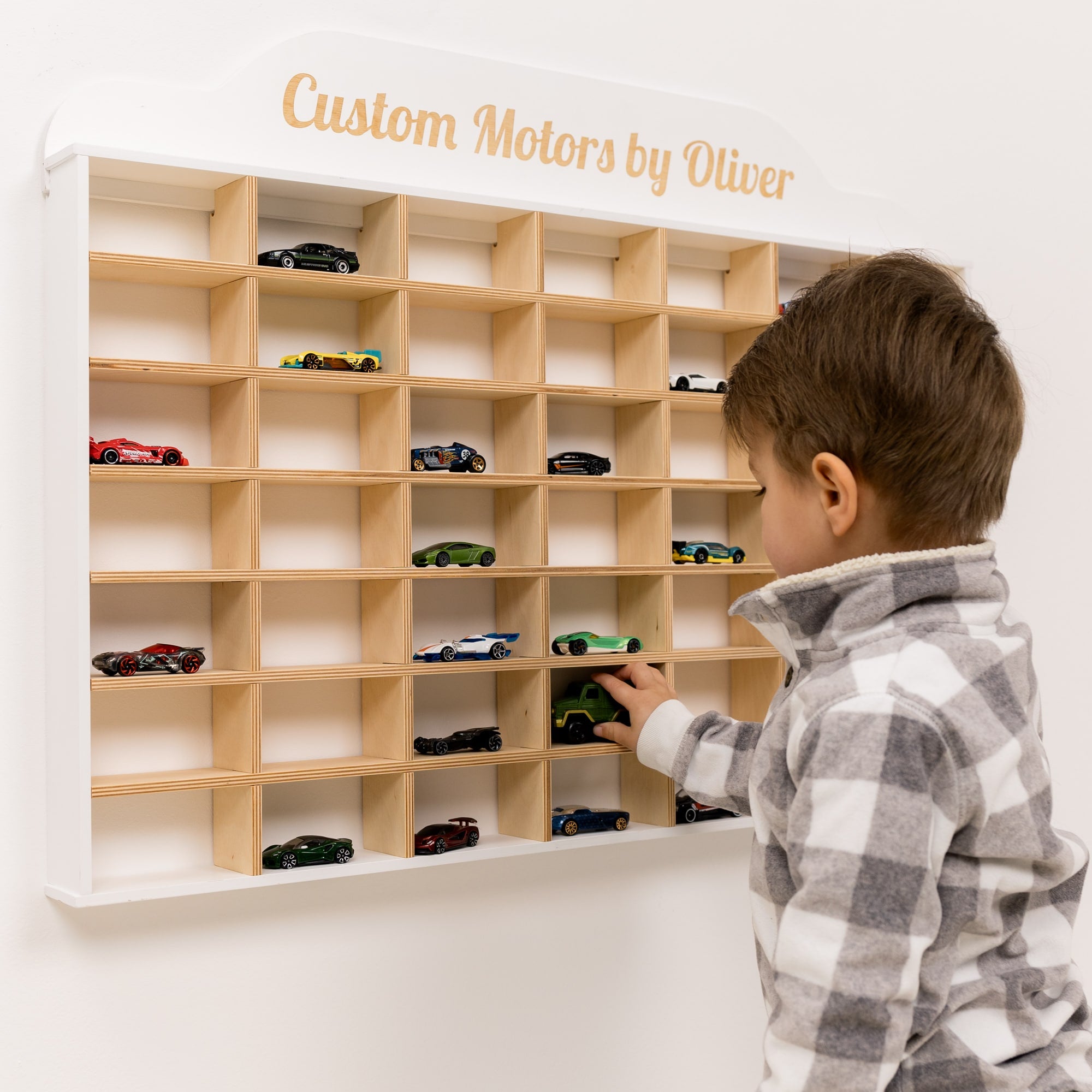 Child playing with a wooden toy car display case labeled 'Custom Motors by Oliver'.