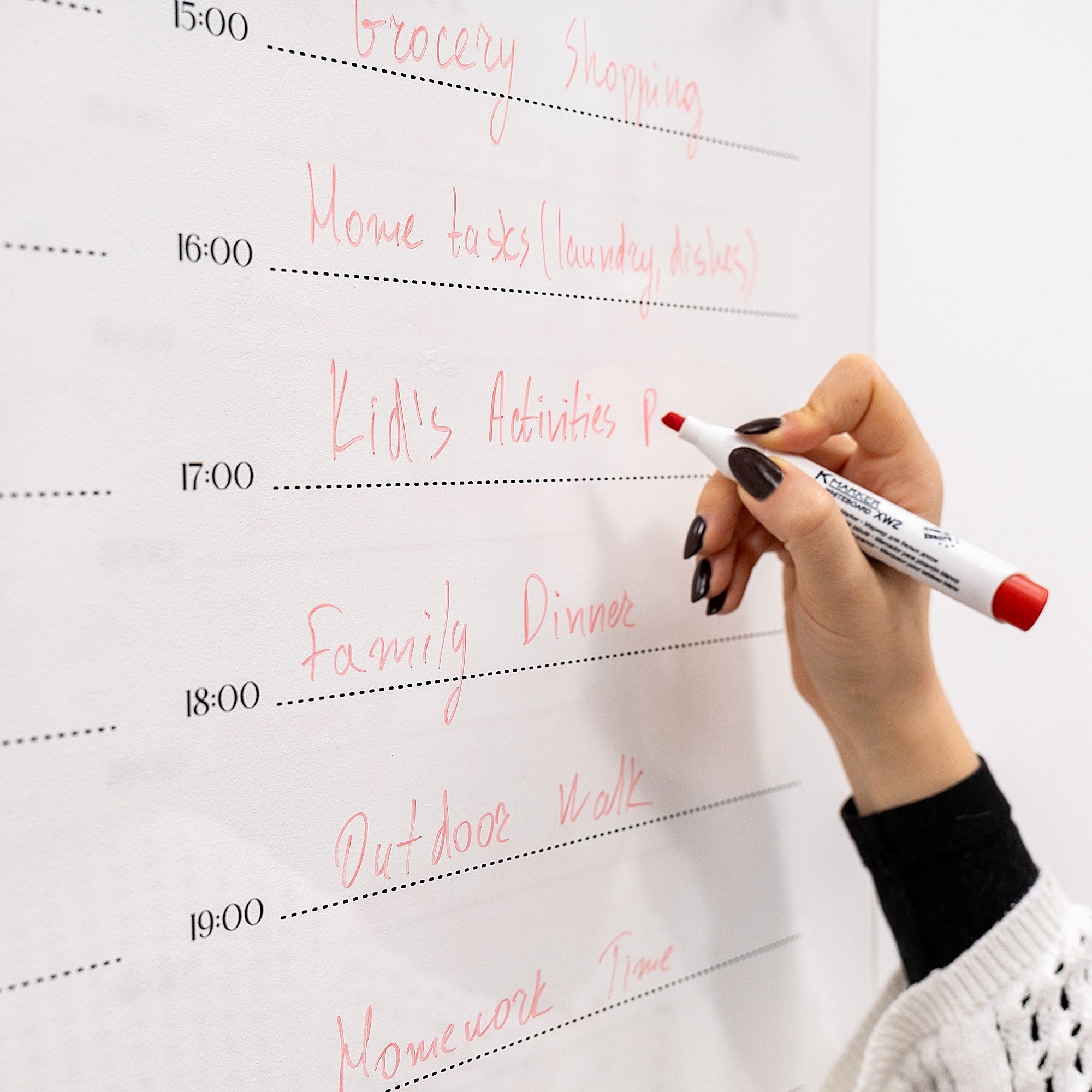 Hand writing a schedule on a whiteboard with a red marker