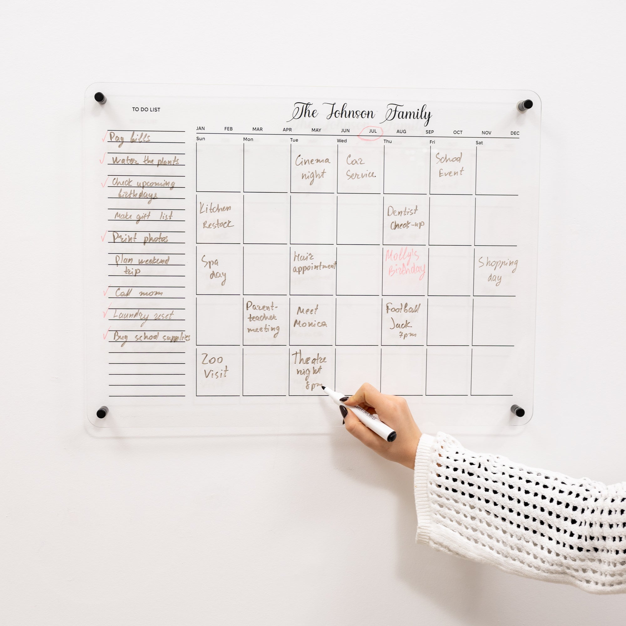 Family calendar on a white wall with a hand holding a marker.