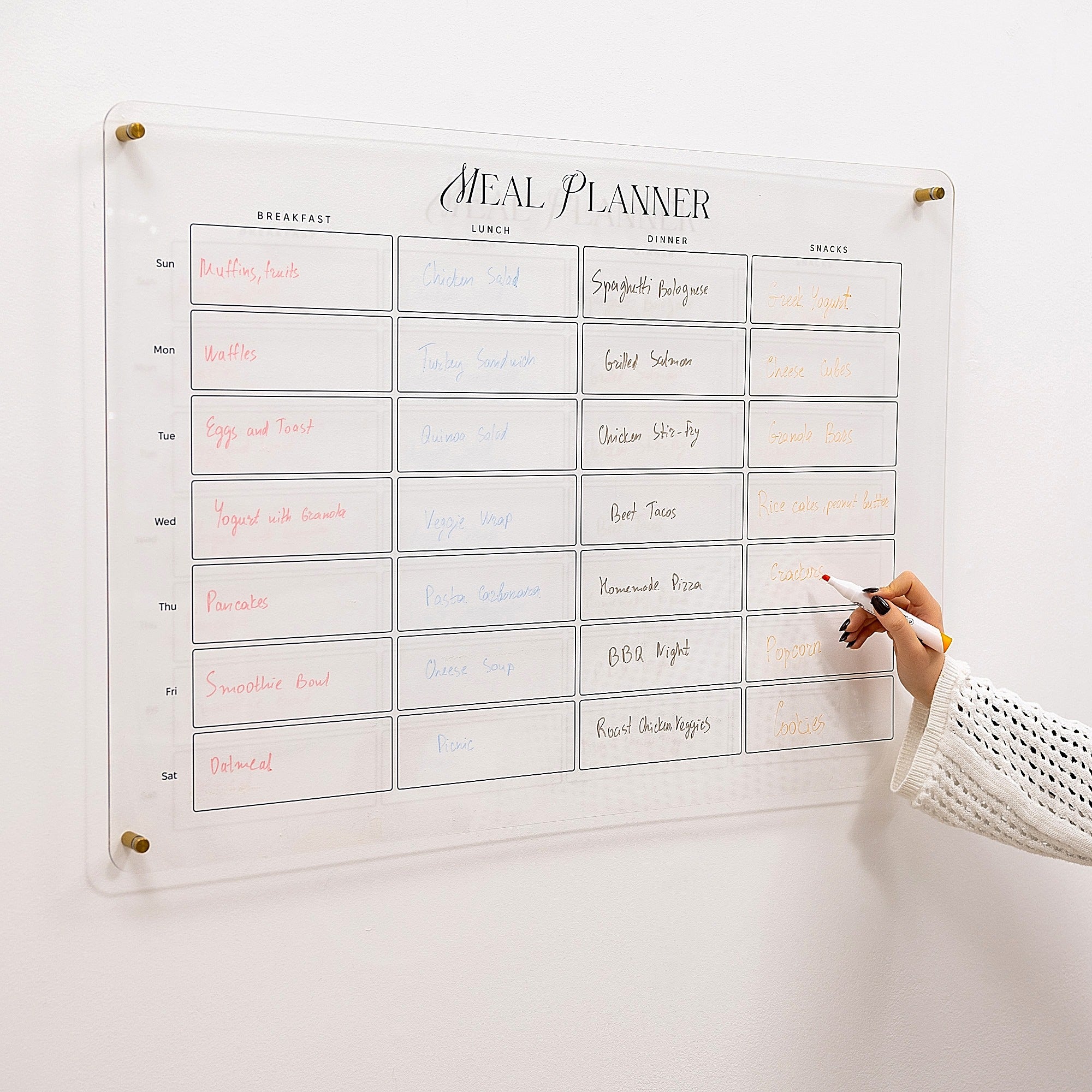 Meal planner with handwritten meals on a white wall, with a hand holding a marker.