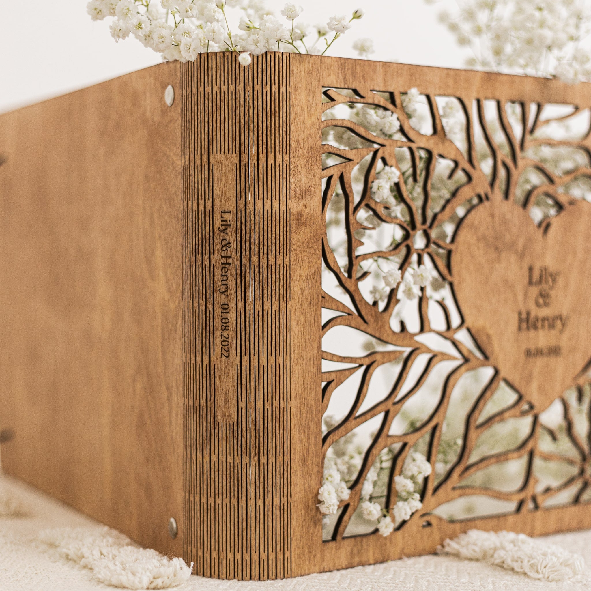 Wooden box with laser cut design and engraved text, surrounded by white flowers.