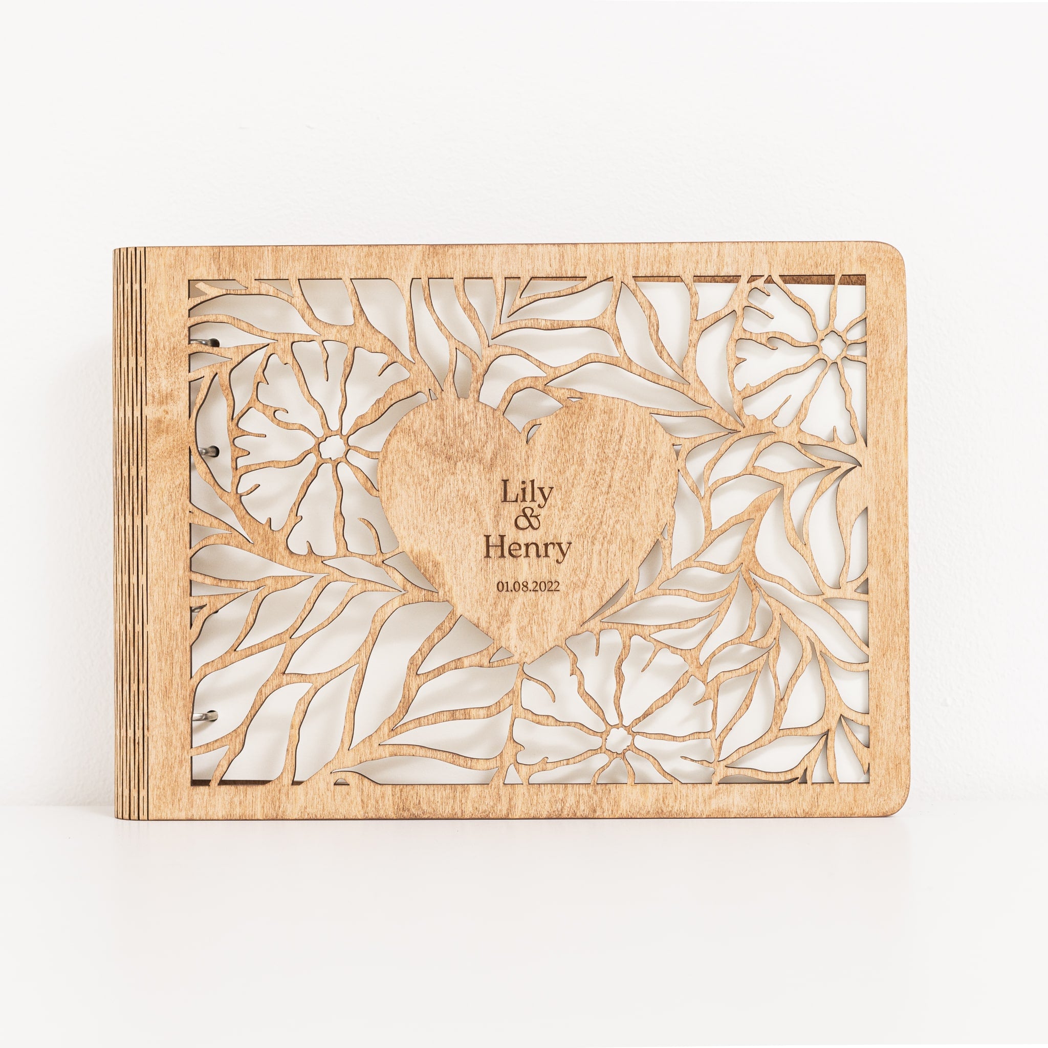 Wooden photo album with floral cutout design and engraved text on a white background