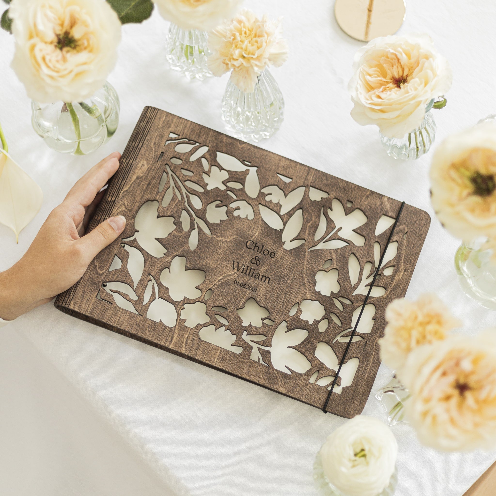 Wooden album with floral cutout design on a white surface with flowers around