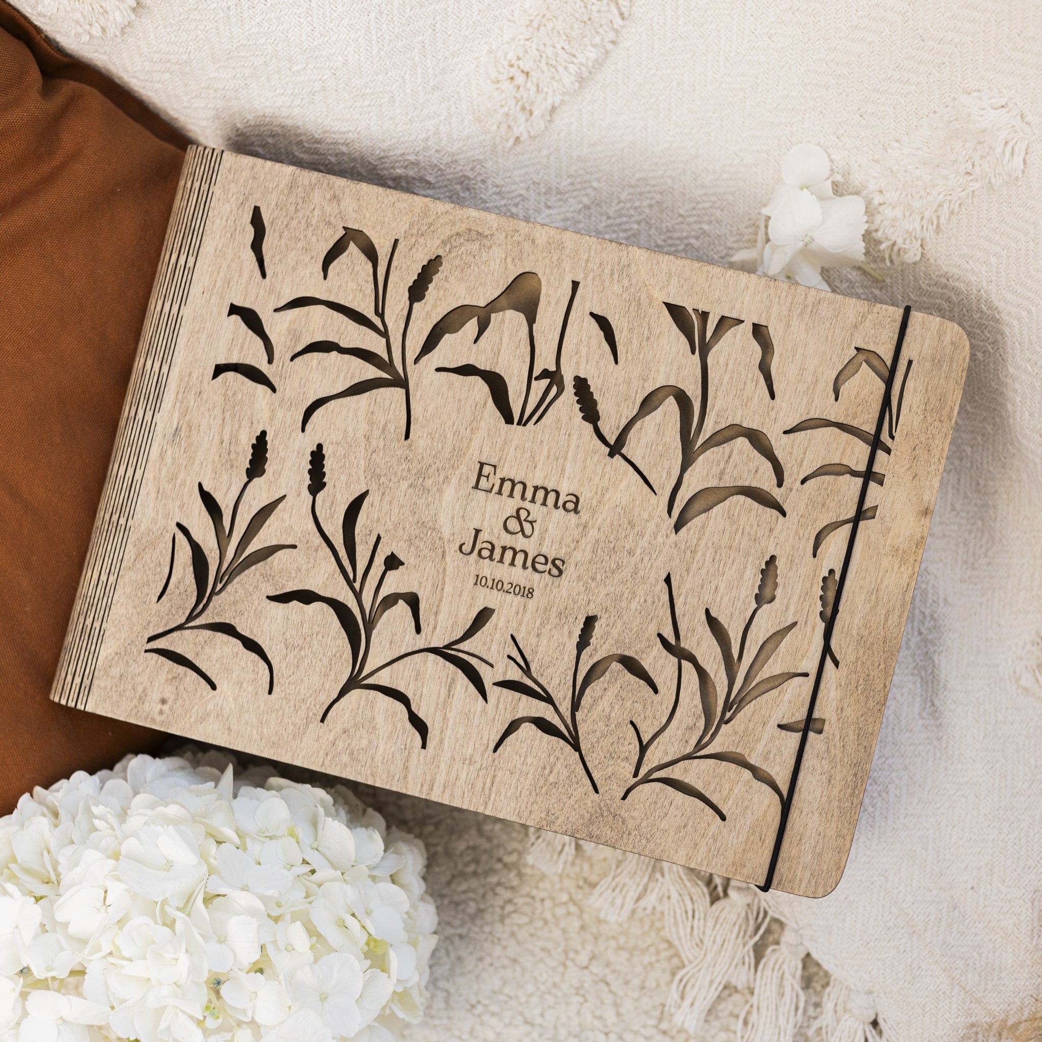 Wooden box with floral design and engraved text 'Emma & James' on a soft fabric background.