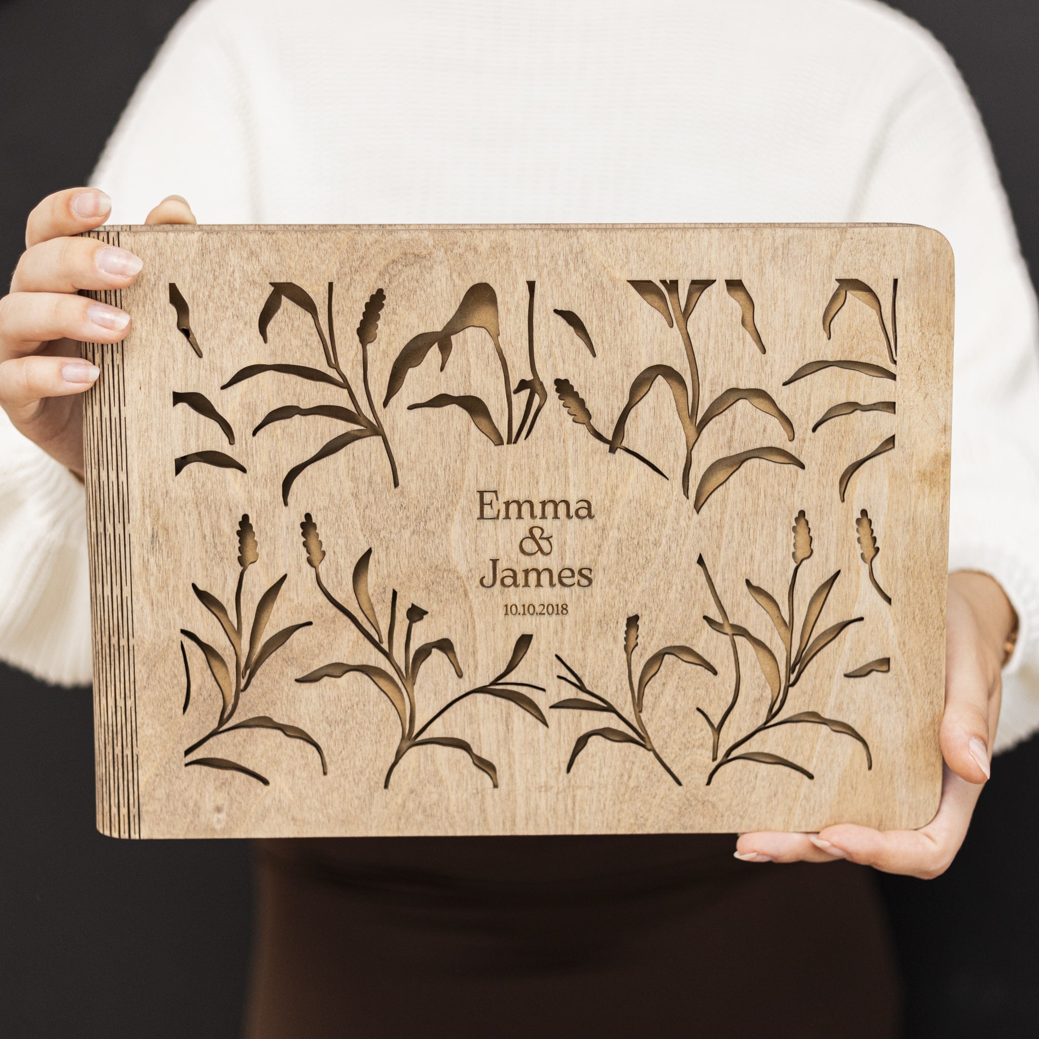 Wooden board with engraved floral patterns and 'Emma & James' text held by a person.