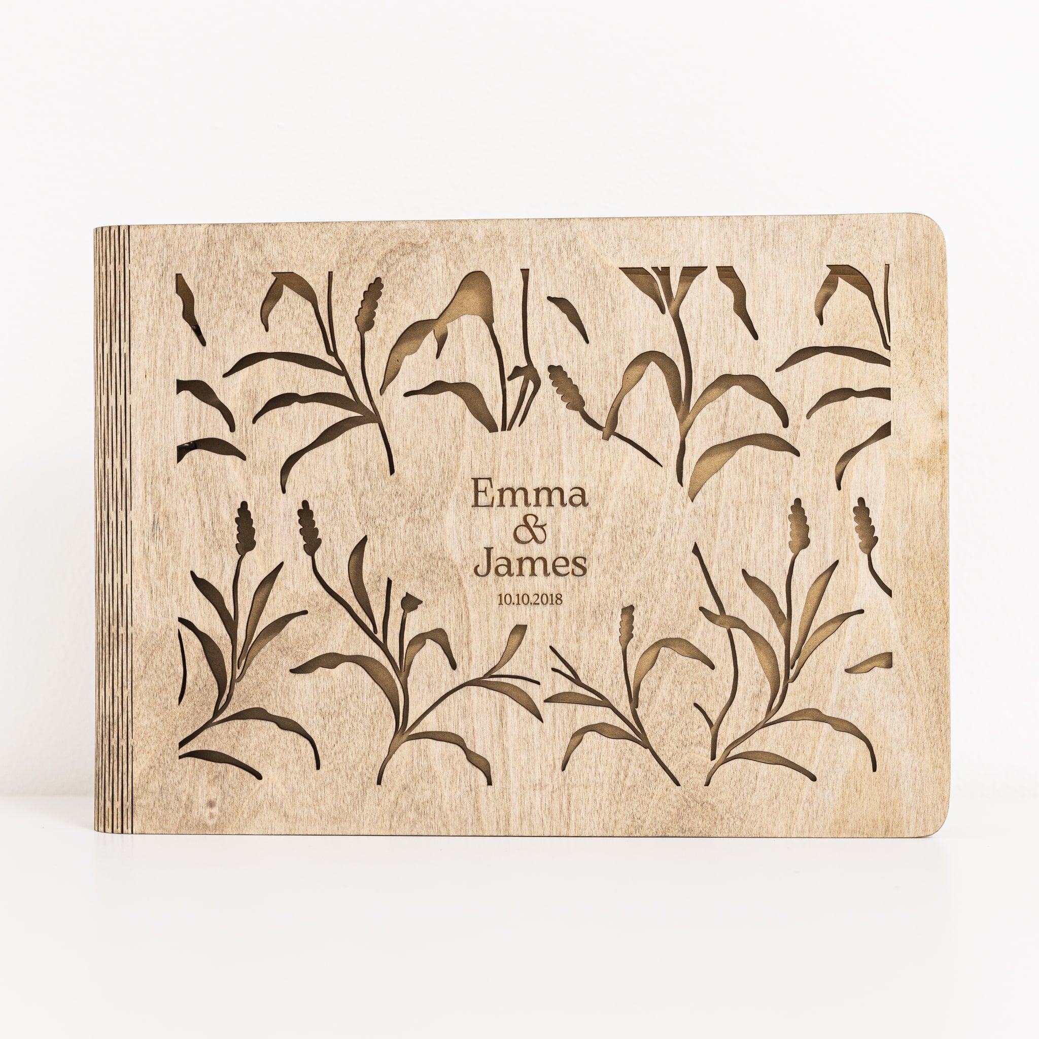 Wooden book with engraved floral design and 'Emma & James' text on a white background