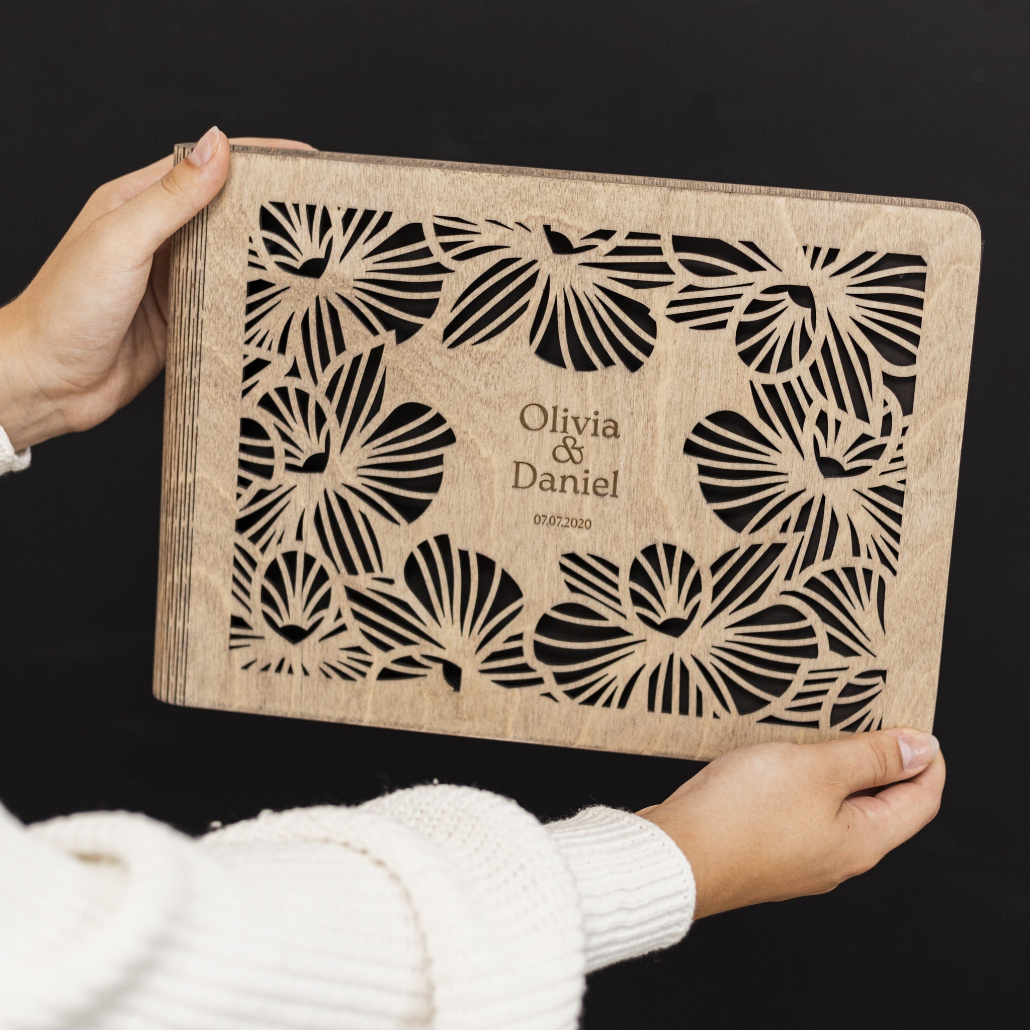 Wooden clutch with laser-cut butterfly design and engraved text held by a person against a black background