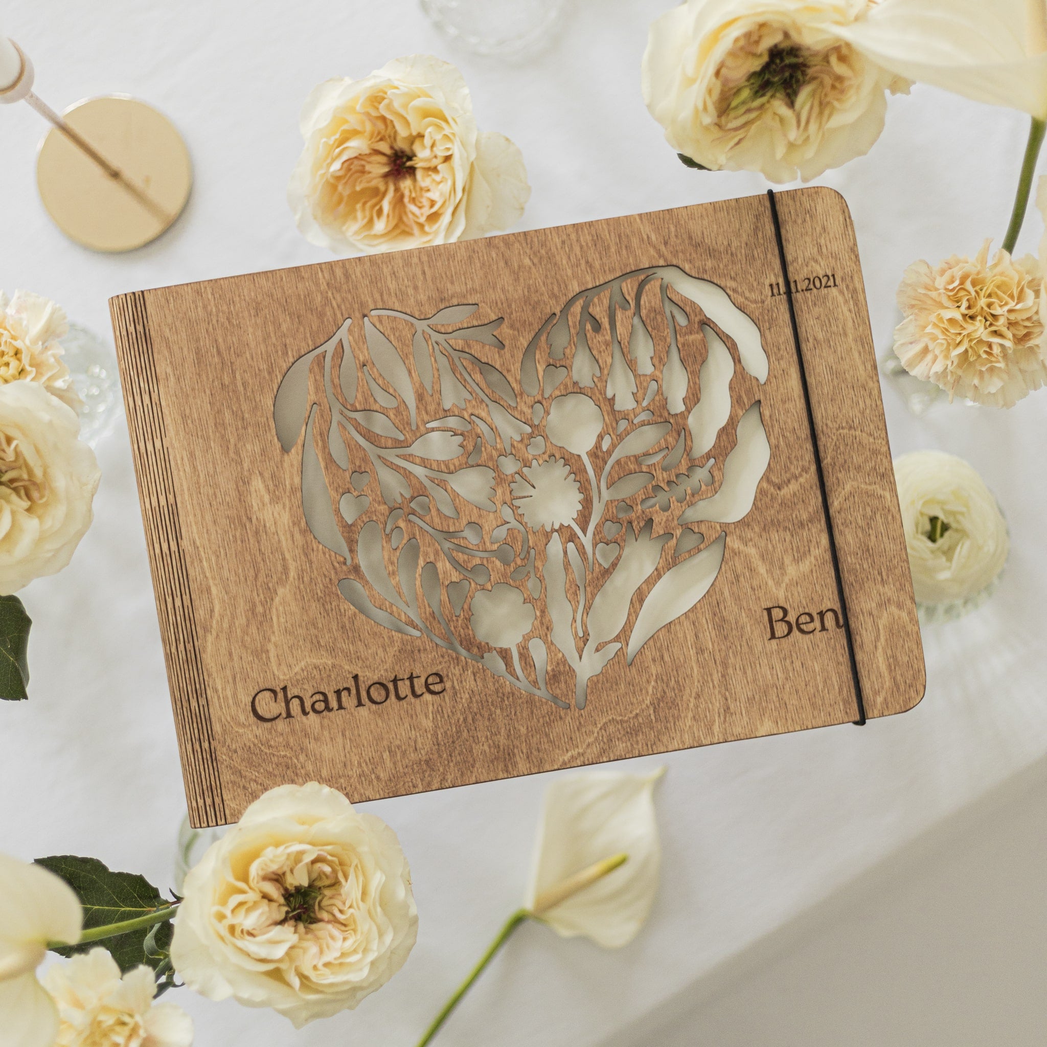 Wooden notebook with floral design and engraved names surrounded by white flowers