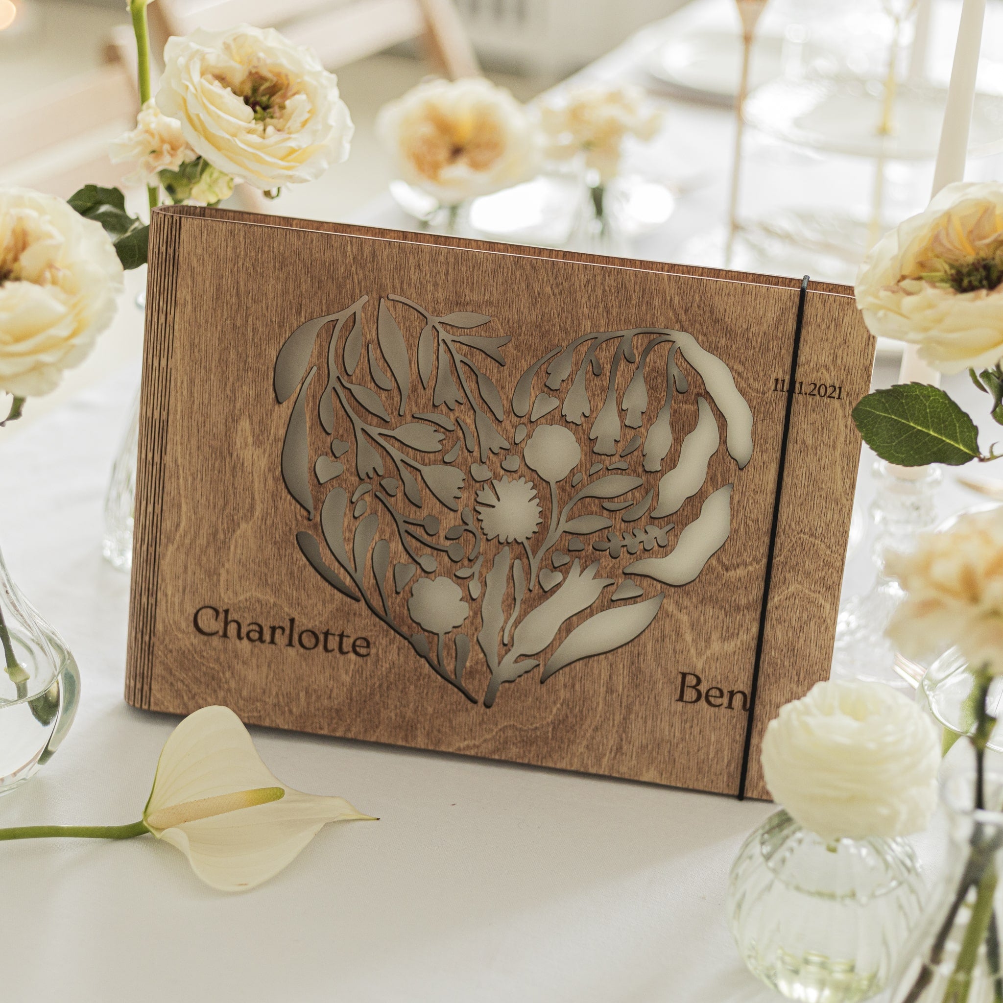 Wooden box with floral design and engraved names on a table with flowers