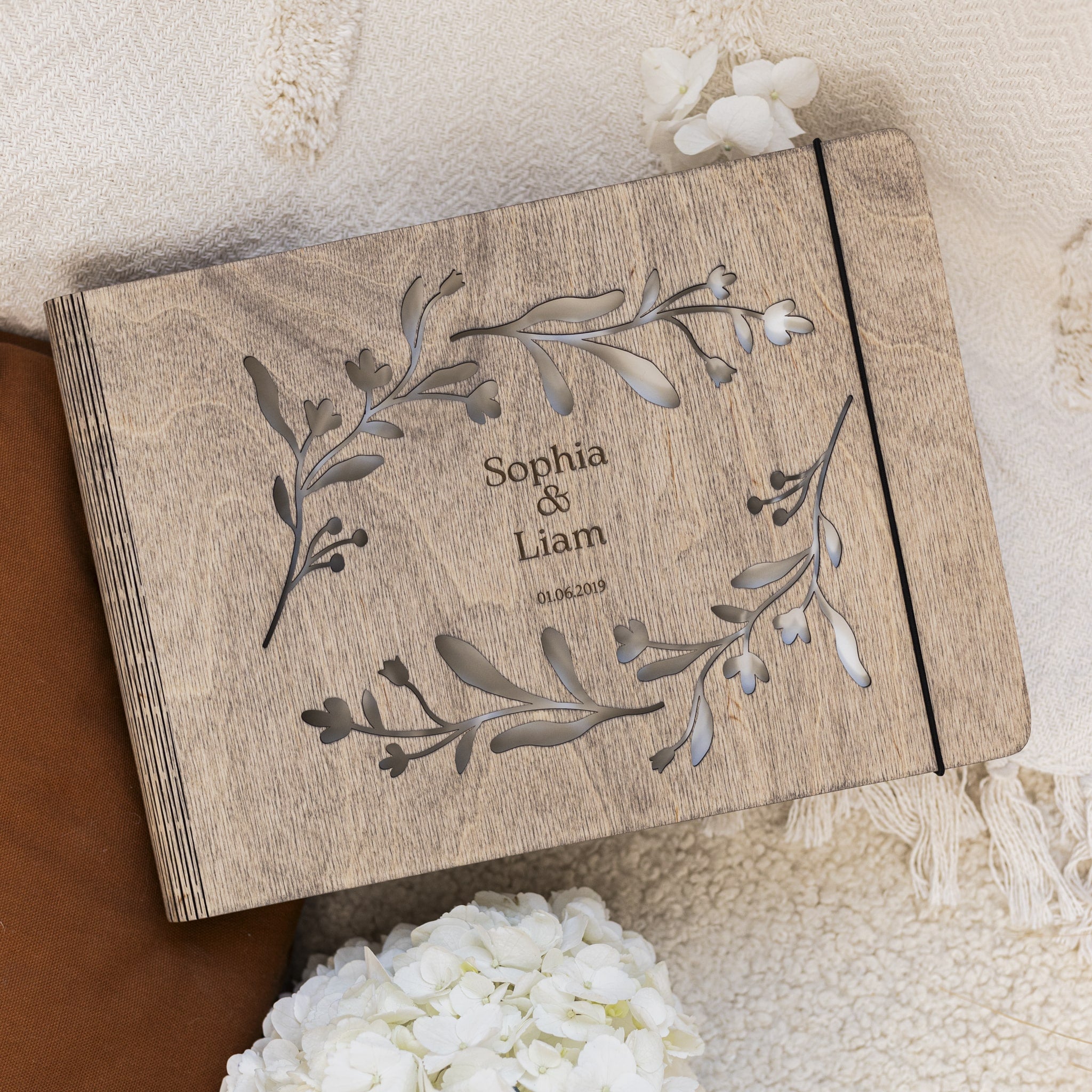 Wooden box with engraved names and floral design on a soft fabric background