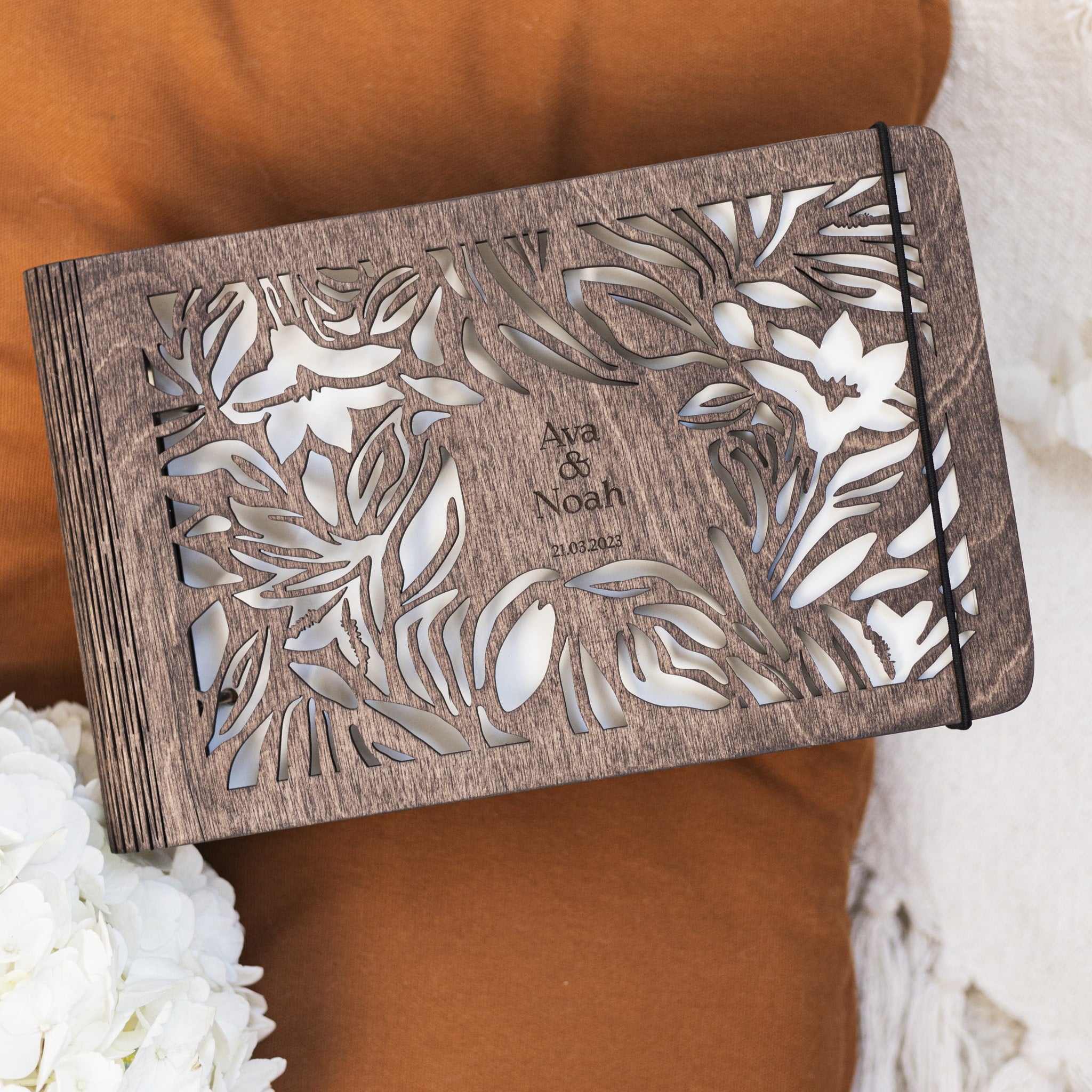 Wooden photo album with floral designs and 'Ava & Noah' text on a brown fabric background.