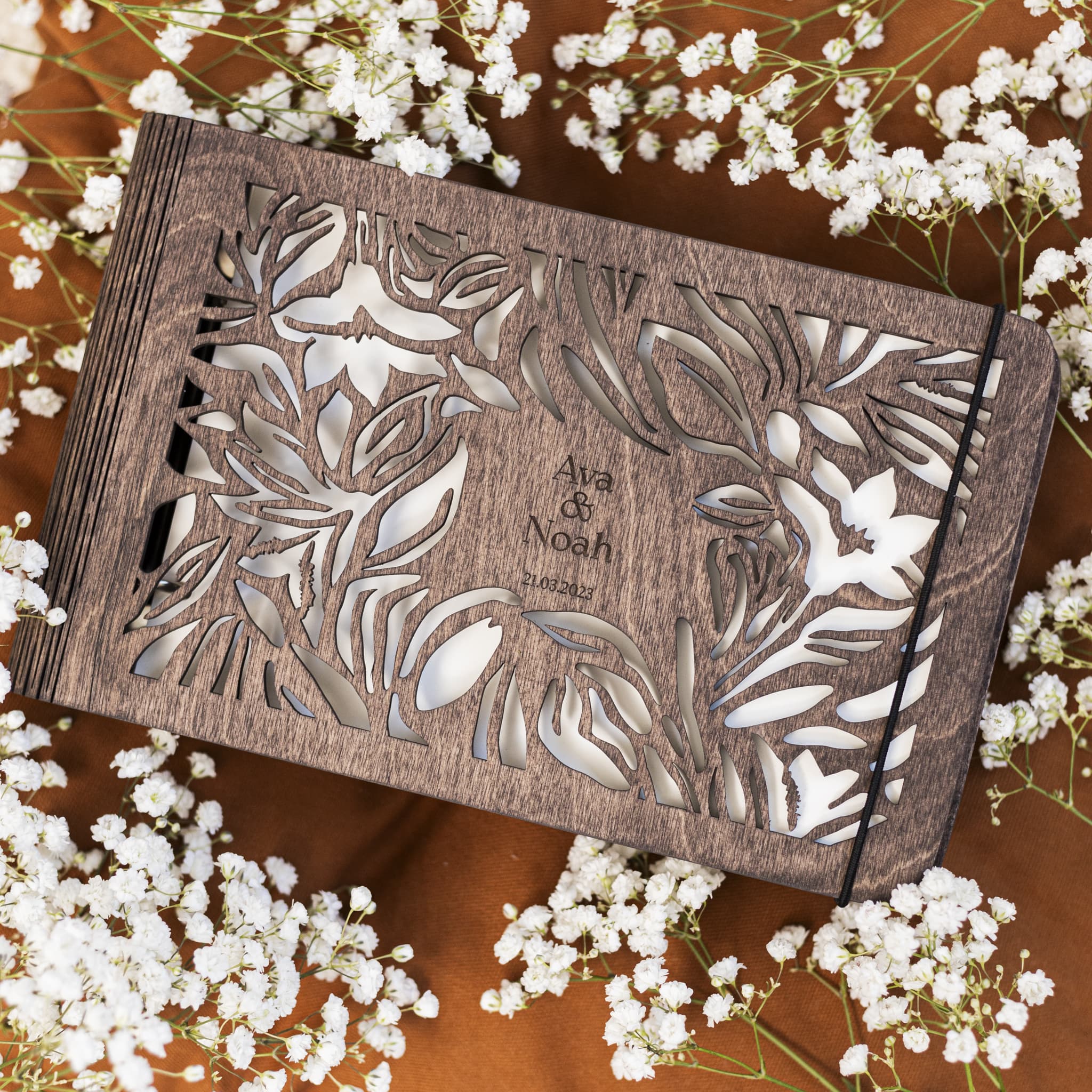 Wooden box with floral patterns and 'Ava & Noah' engraving on a wooden surface with white flowers.