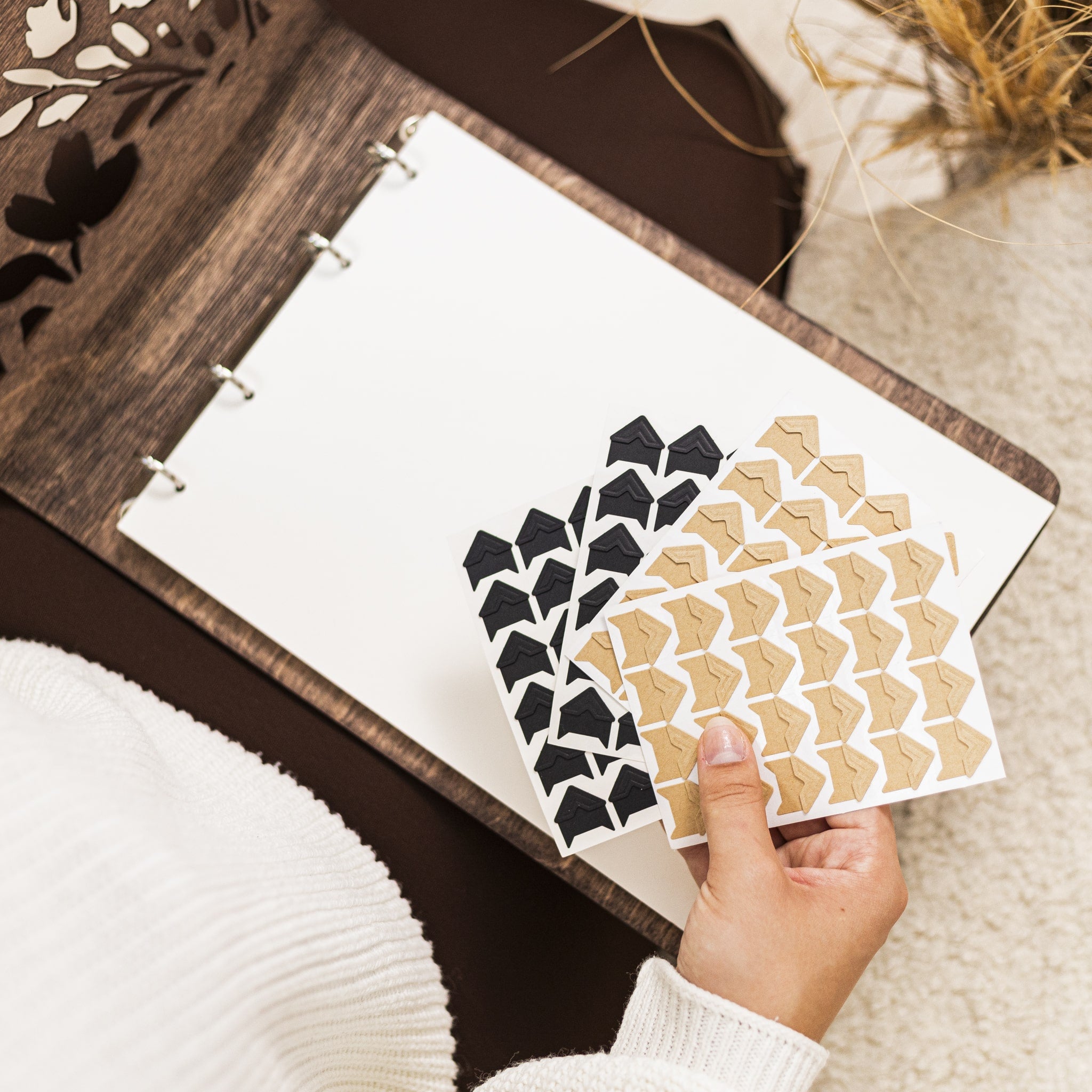 Hand holding a sheet of black and beige geometric patterned stickers over an open notebook.