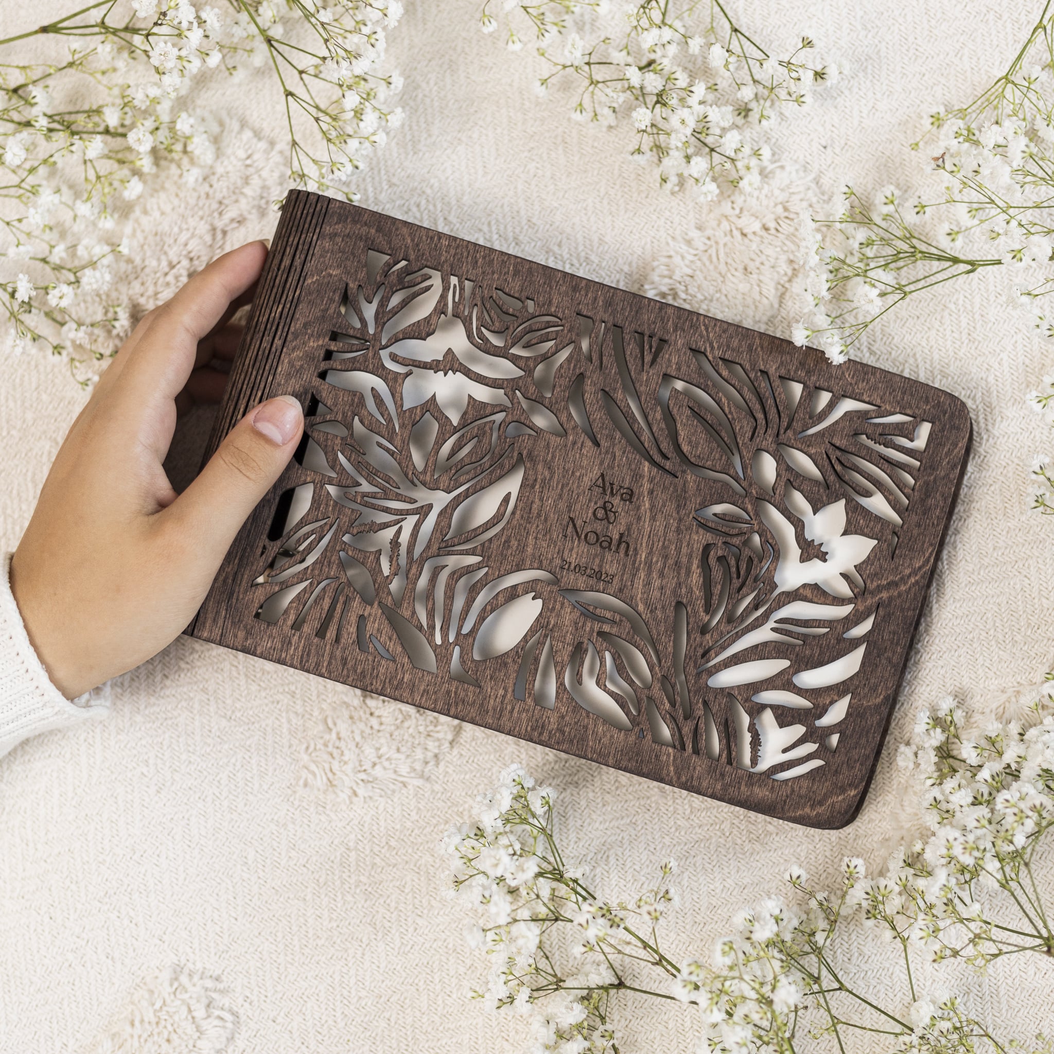 Wooden wallet with floral cutout design held by a hand on a light background with flowers.