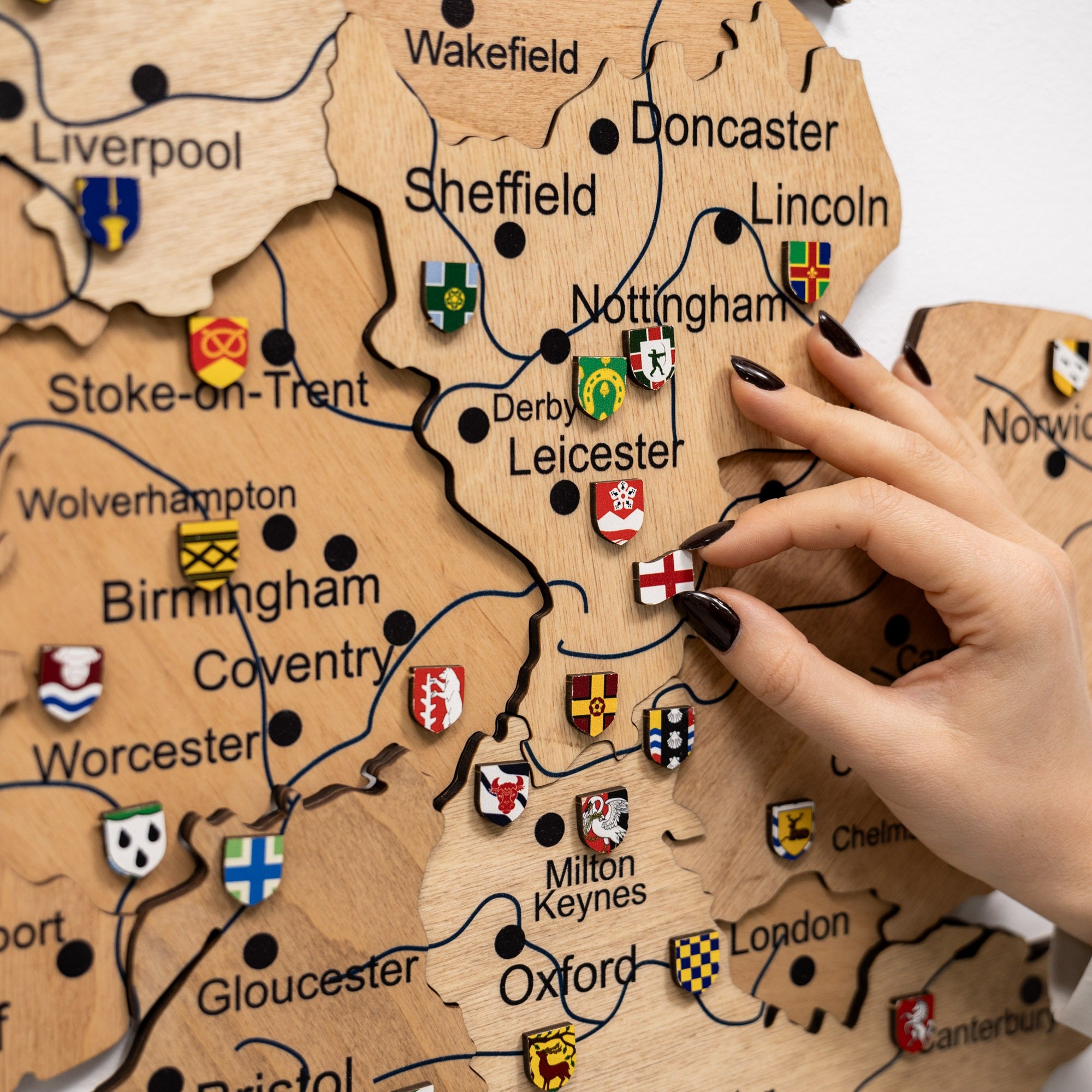 Wooden map of the United Kingdom with city names and flags, hand placing a flag on the map.