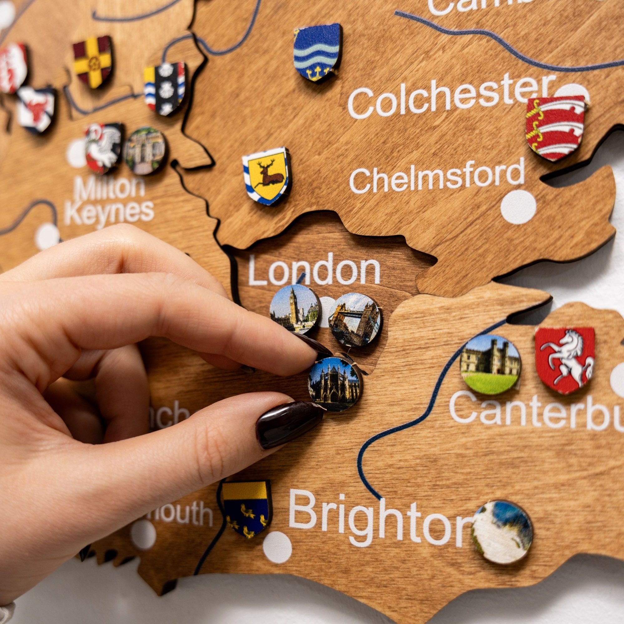 Wooden map of England with pins representing cities and landmarks, hand placing a pin on London.