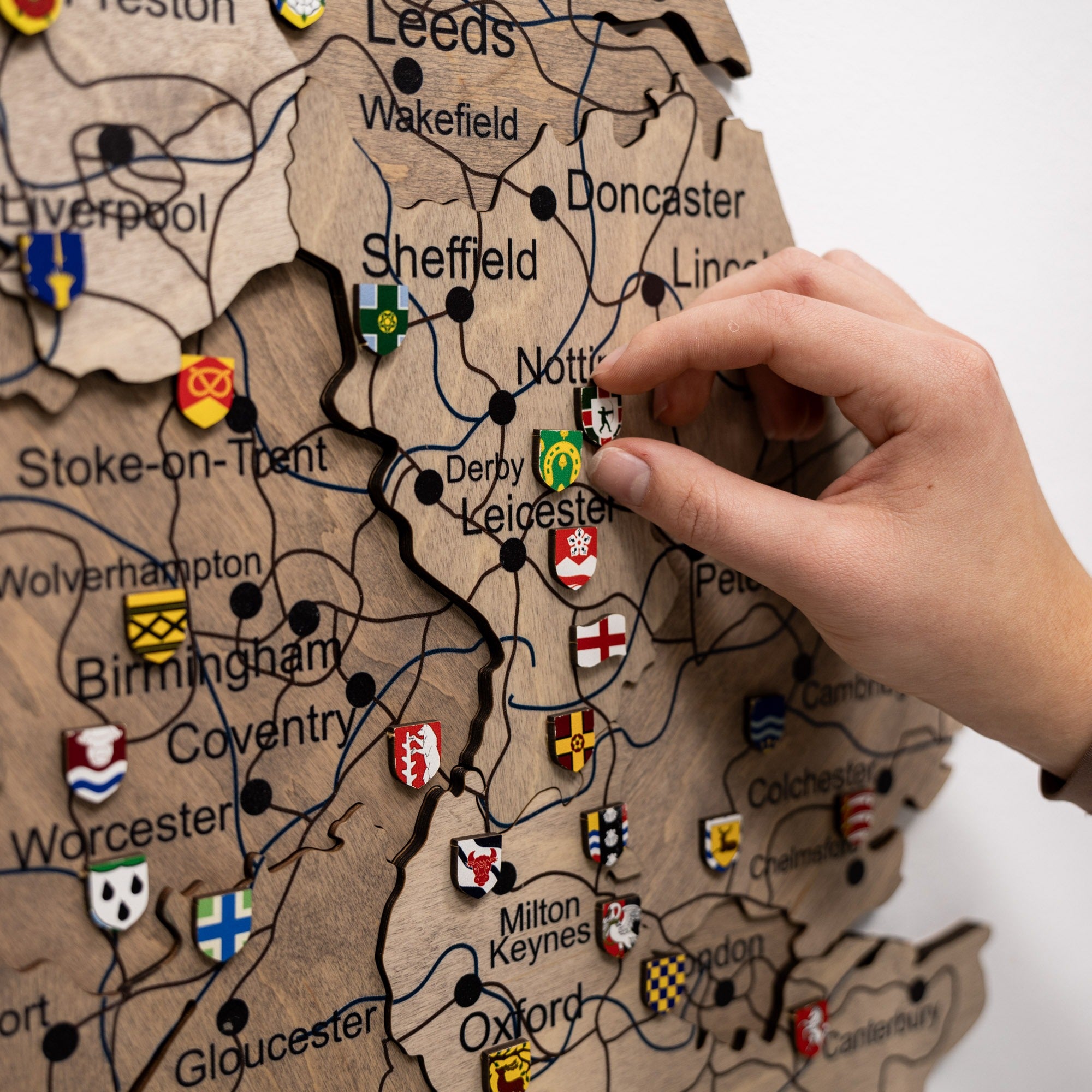 Hand placing a flag emblem on a wooden map of England.