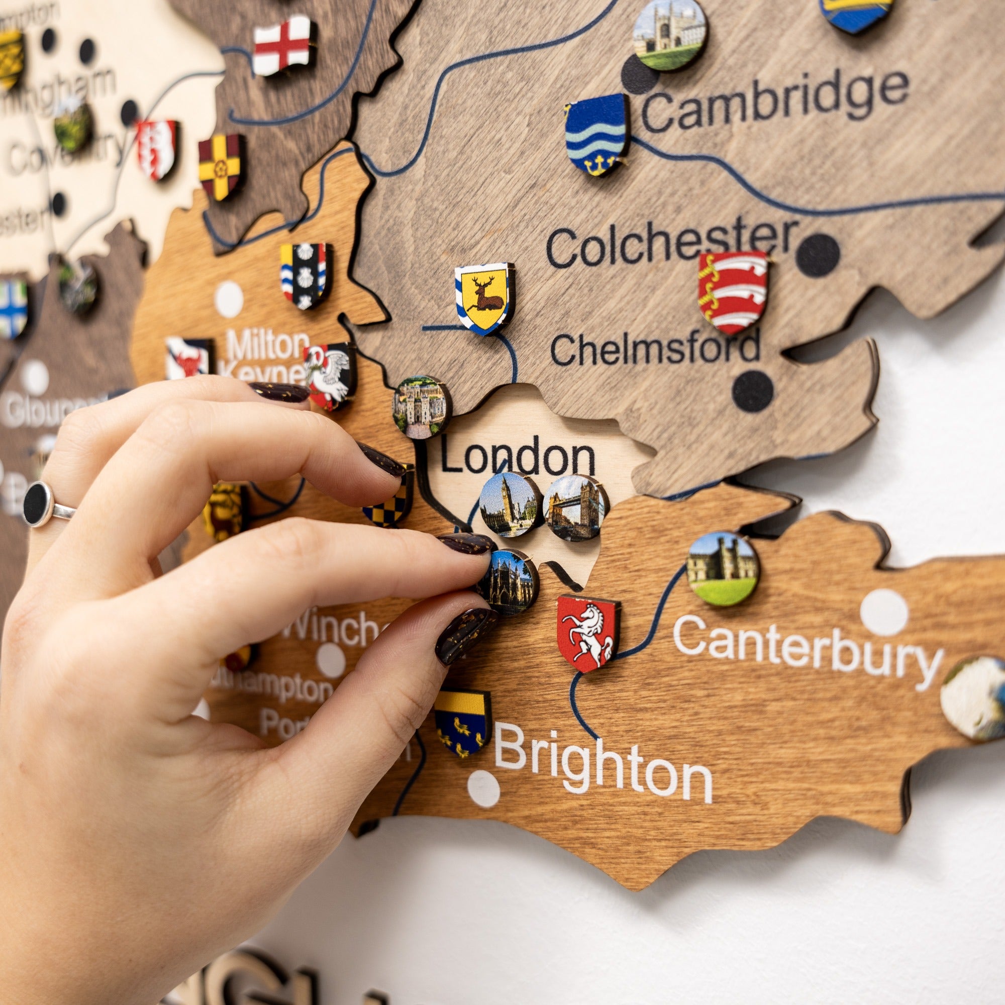 Wooden map of England with pins marking locations, hand placing a pin on London.