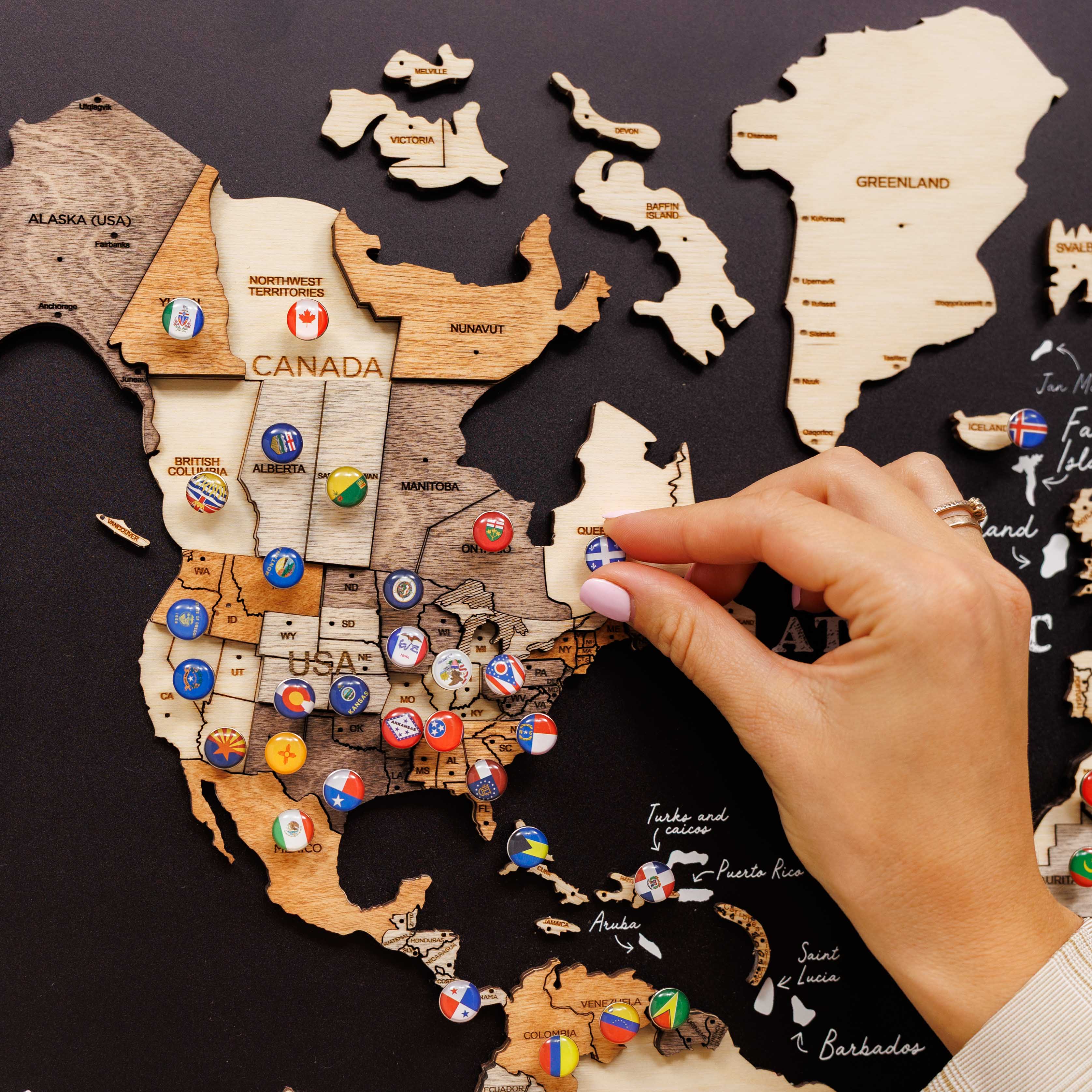 Wooden map puzzle with USA and Canada pieces, hand placing a flag piece.
