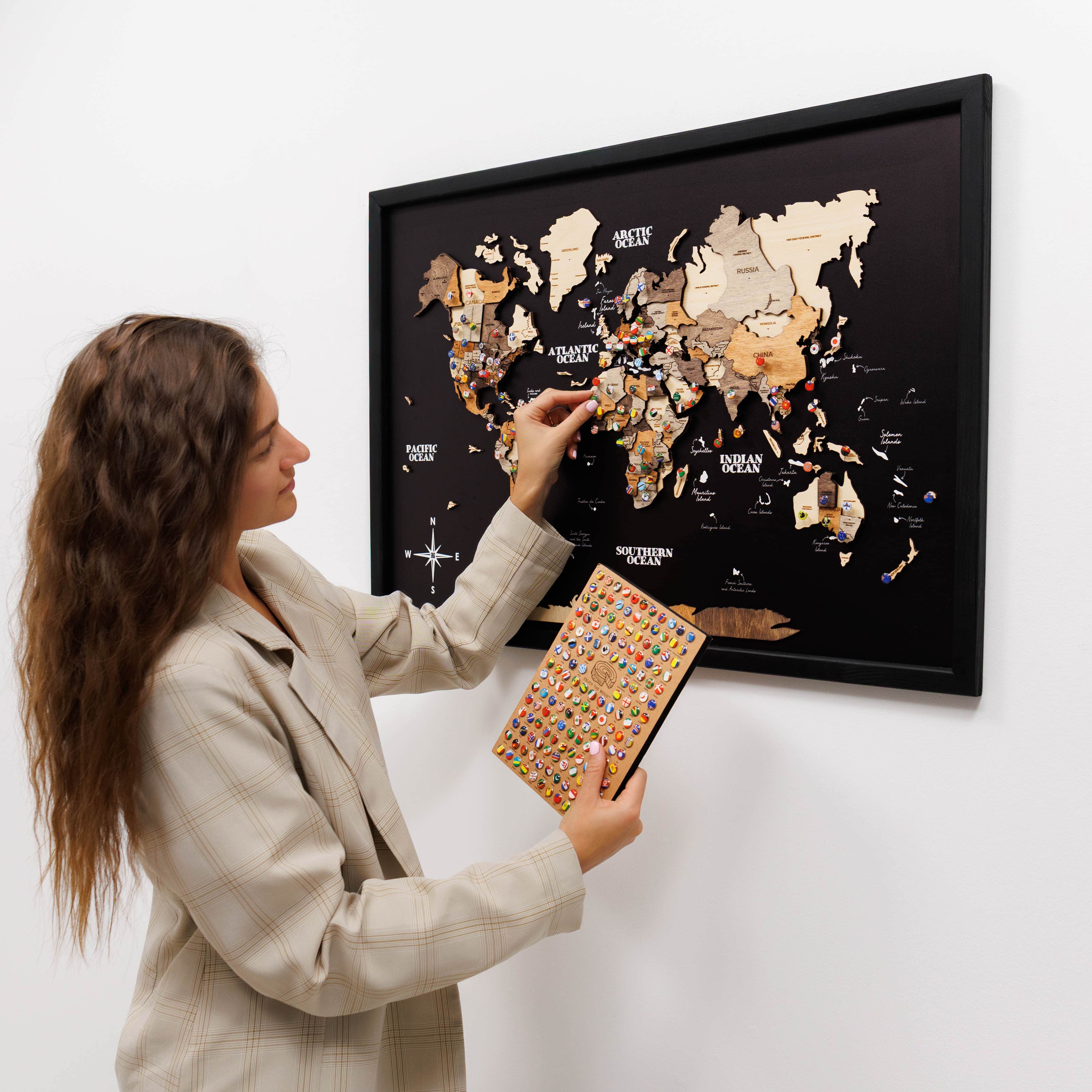 Woman holding a colorful book next to a framed world map on a white wall