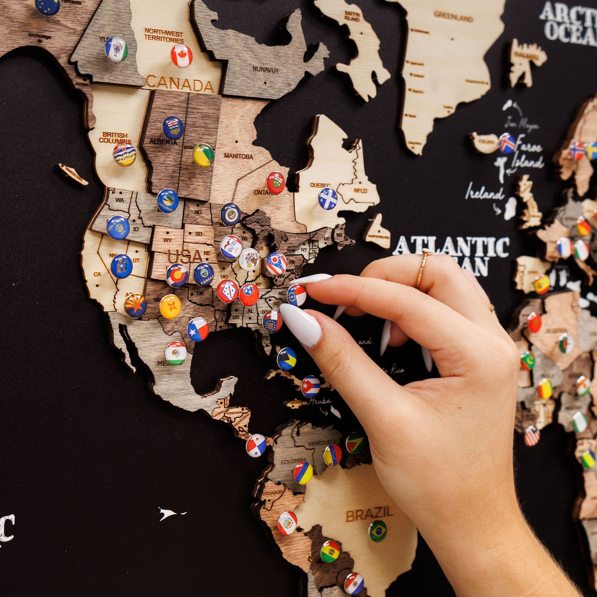 Hand placing a pin on a wooden map of North America with variously colored pins.