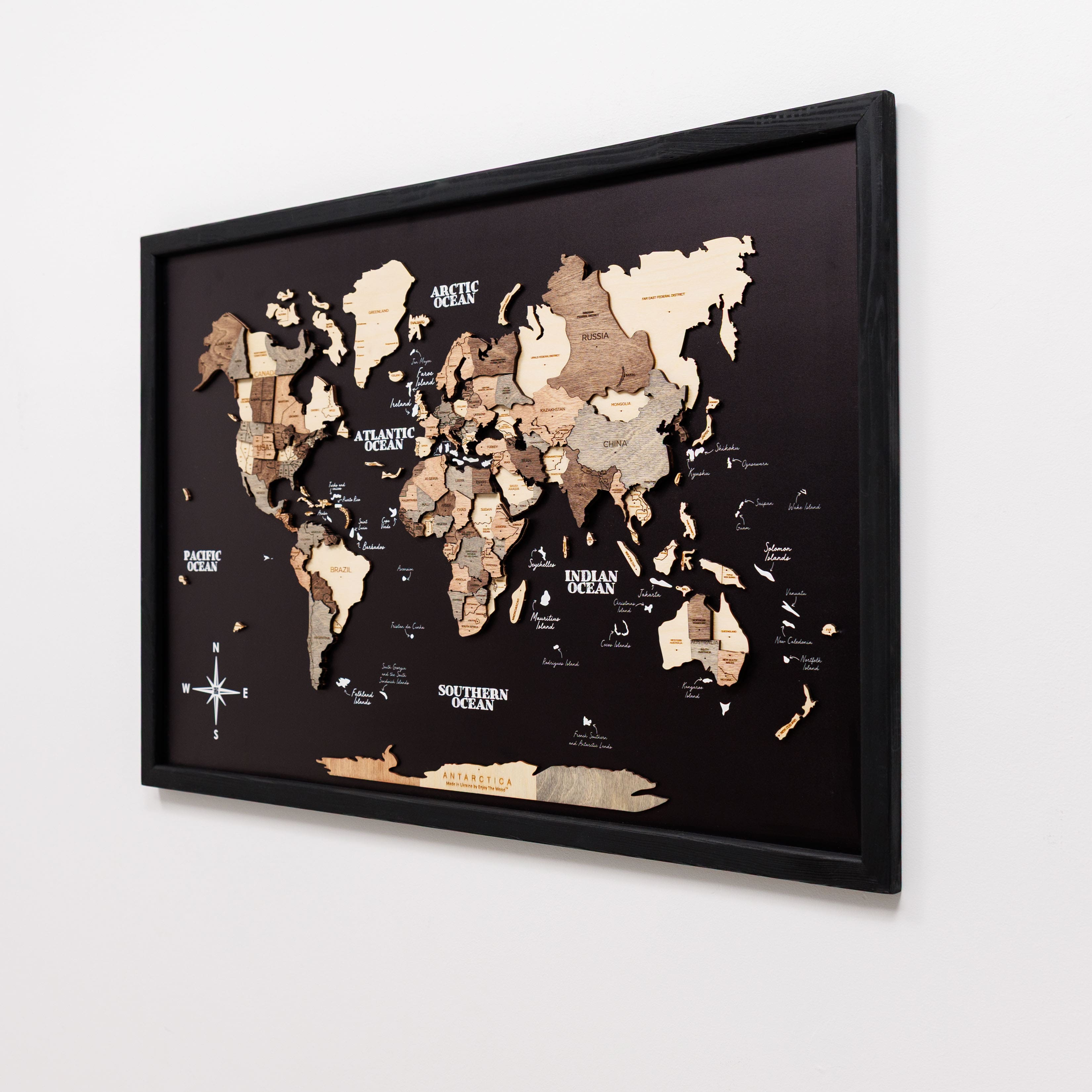 World map with wooden relief design in a black frame on a white wall