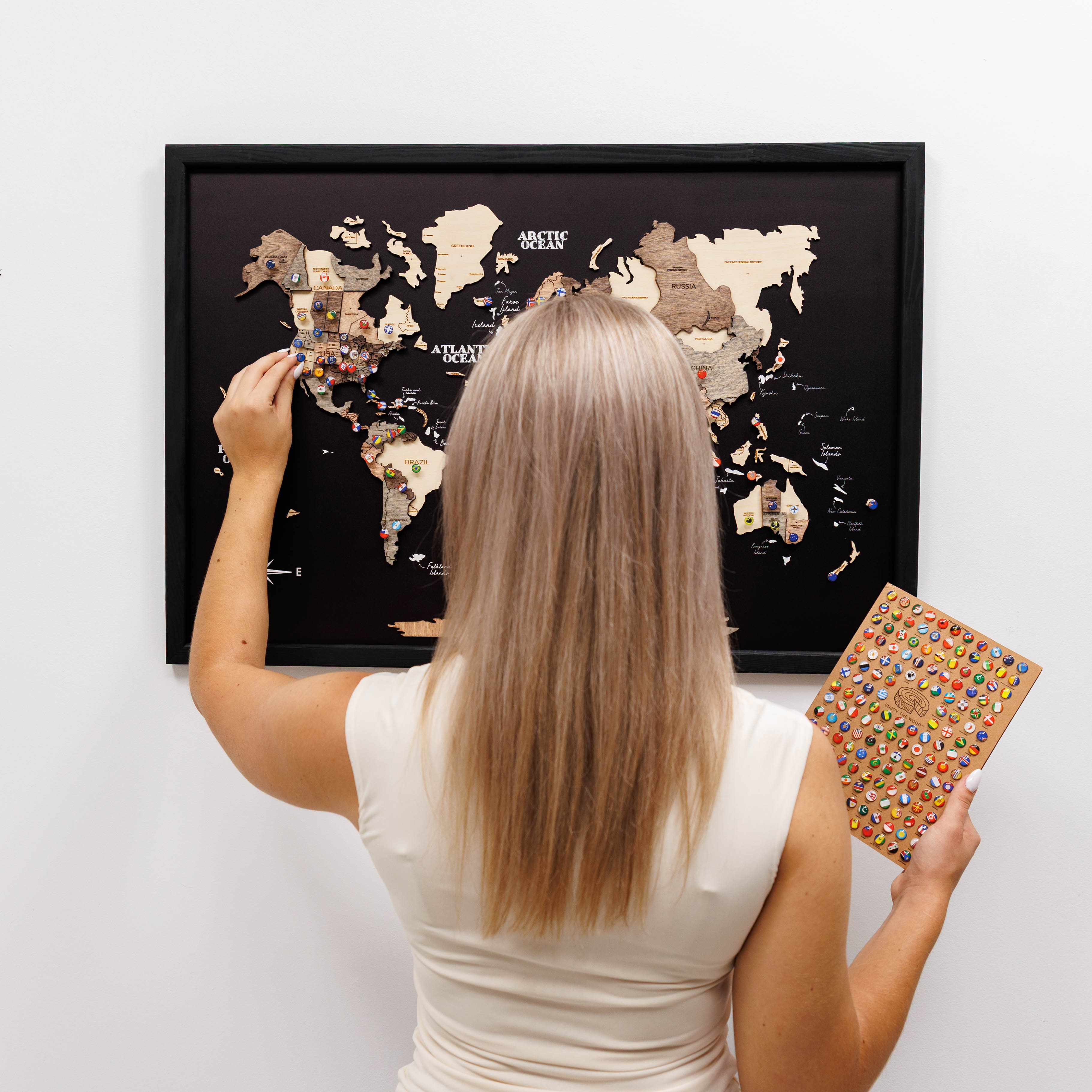 Woman holding a world map with pins and a book against a white wall