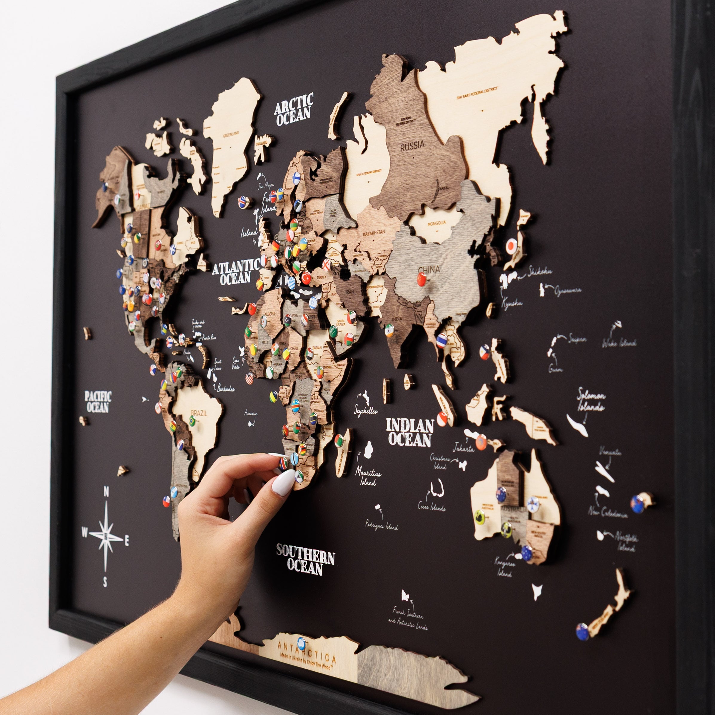 World map puzzle with wooden pieces on a black background, held by a hand.