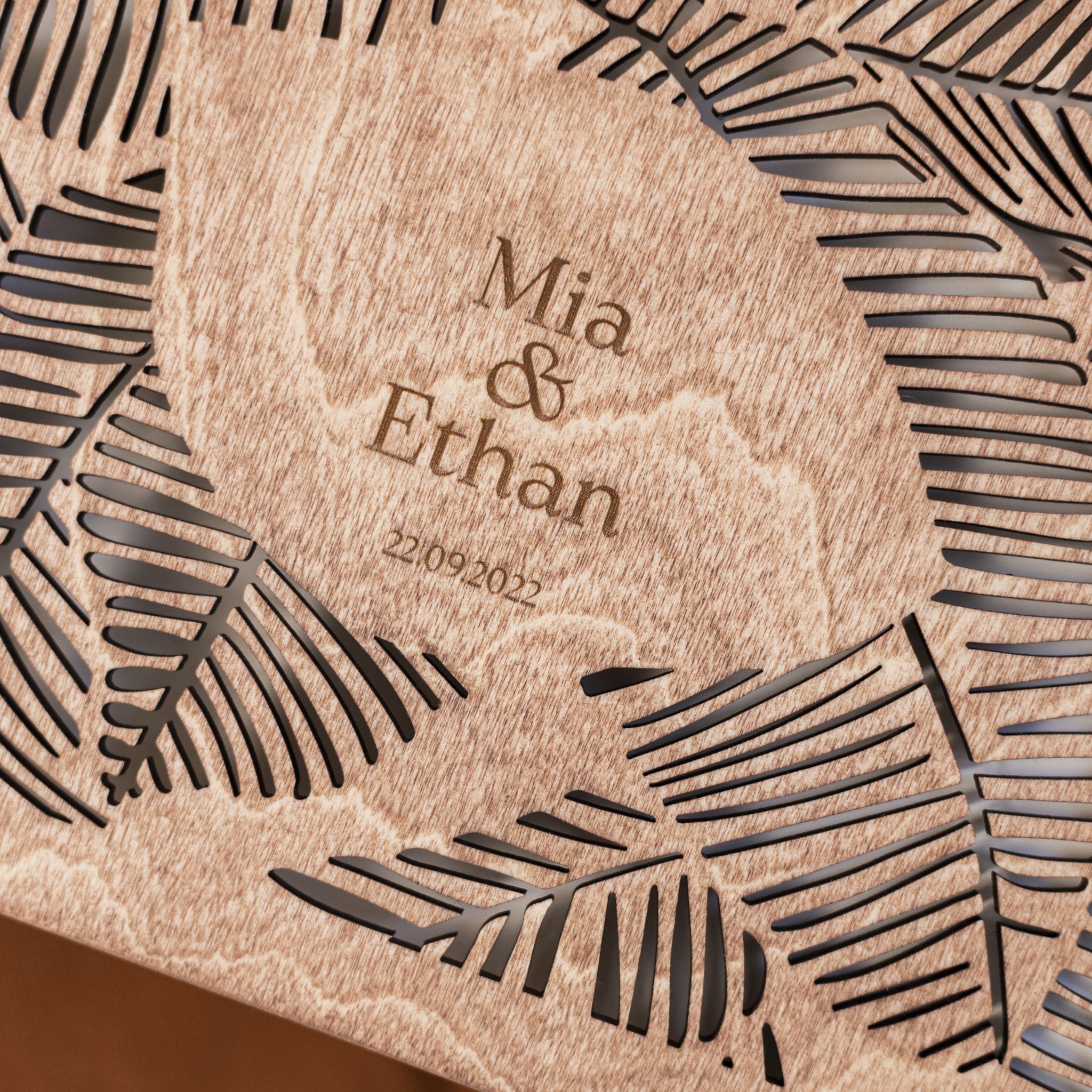 Wooden coaster with engraved names 'Mia & Ethan' and date '22.09.2022', surrounded by leaf patterns.