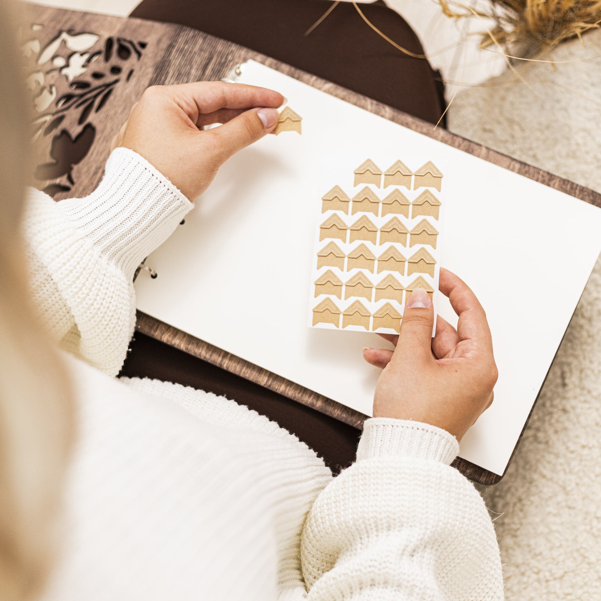 Person holding a sheet of gold house-shaped stickers on a white surface.