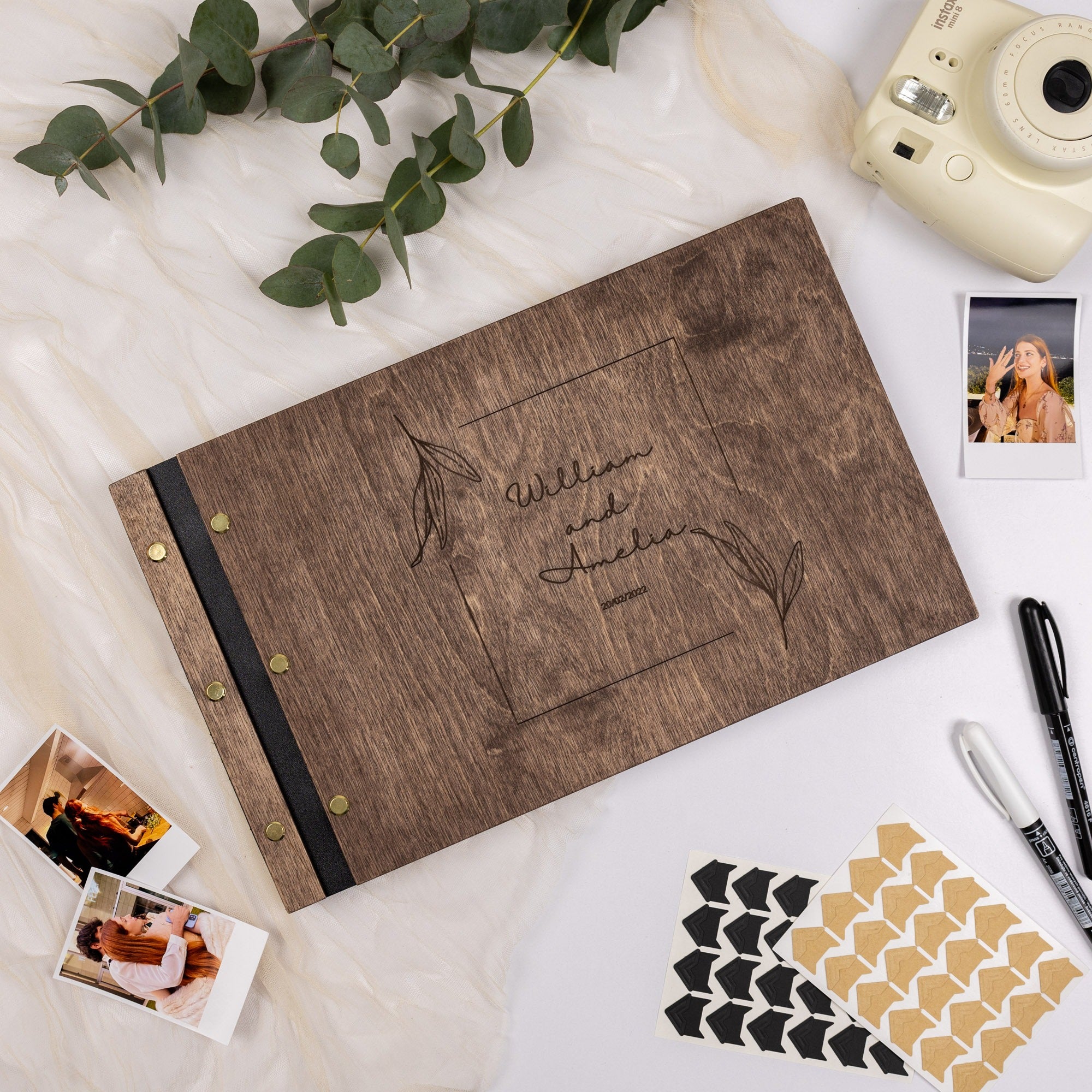 Wooden photo album with engraved design on a white surface with photos and stationery items.