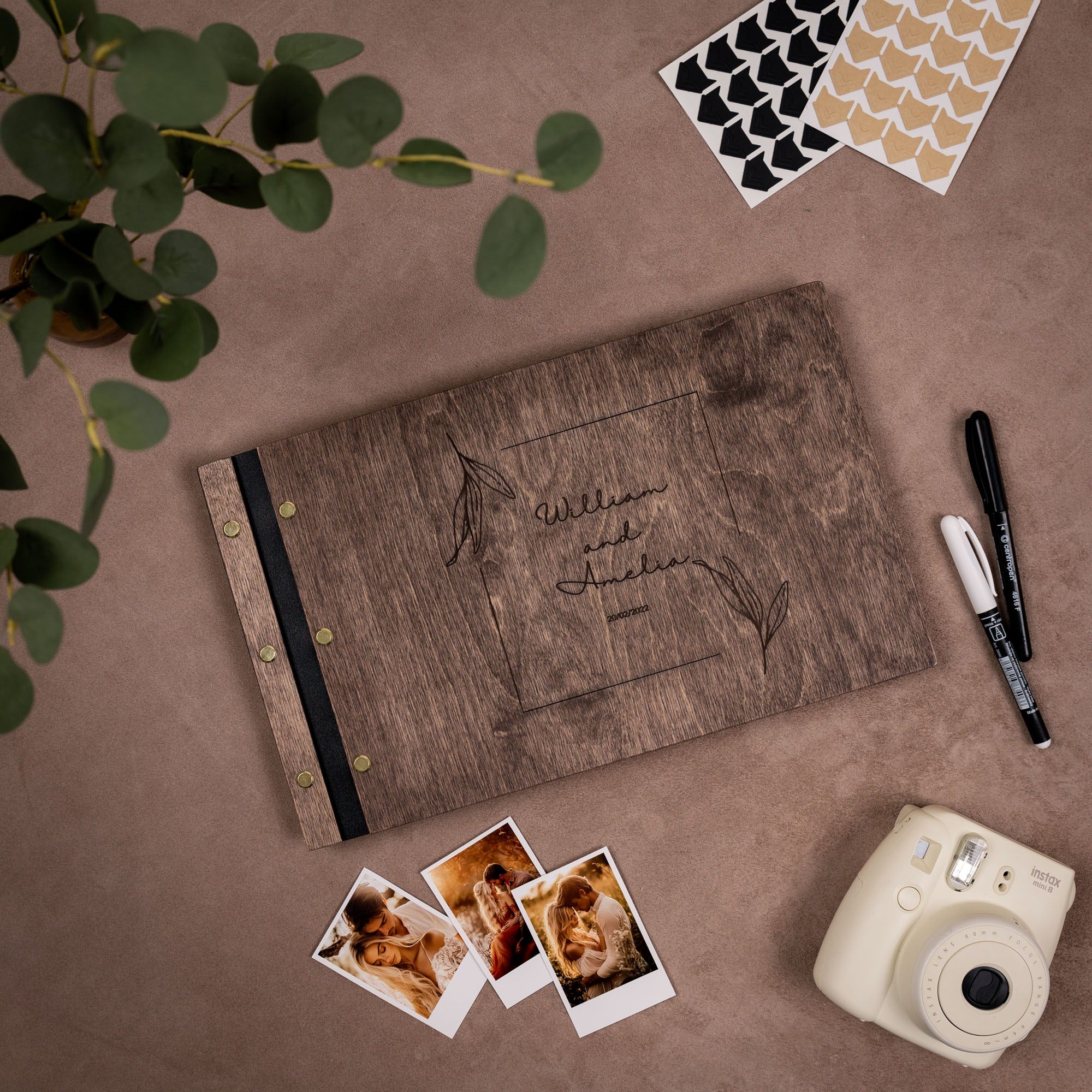 Wooden photo album with engraved names, photos, and a camera on a brown surface.