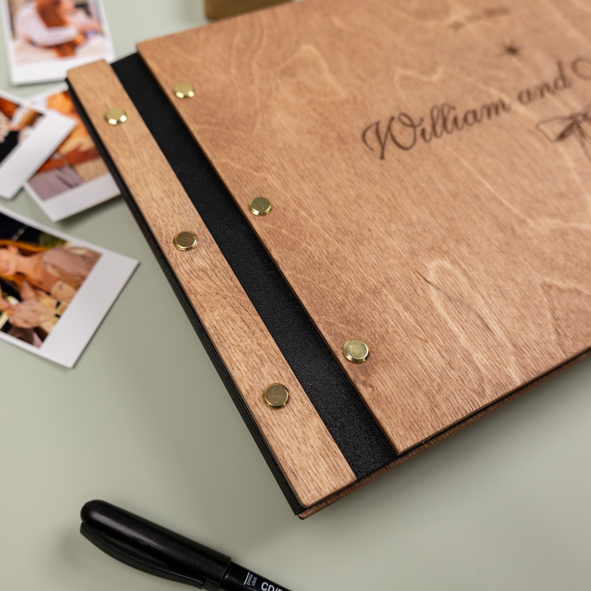 Wooden photo album with 'William and' engraving, surrounded by photos on a light surface.