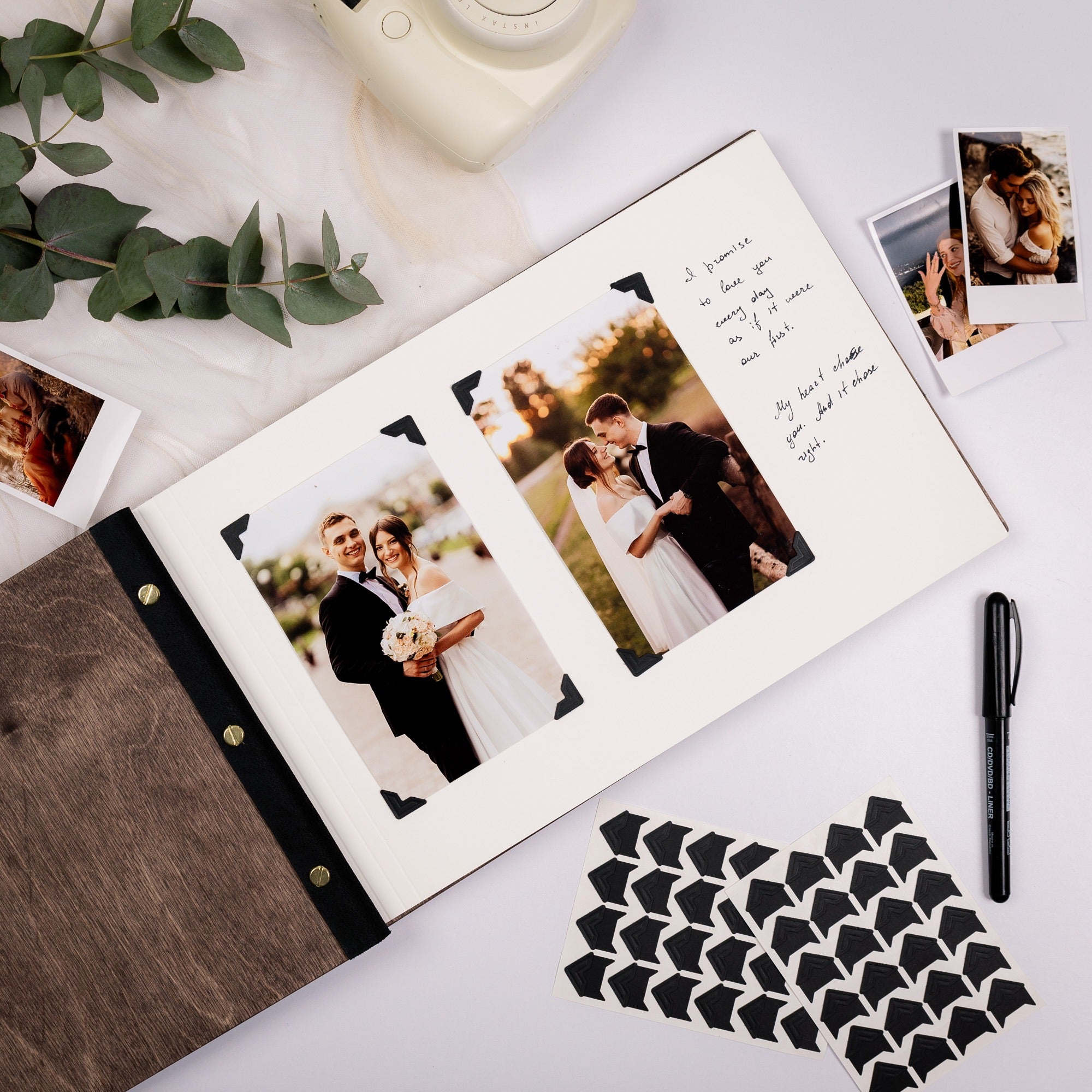 Wedding photo album with couple photos on a white surface with a pen and decorative items.
