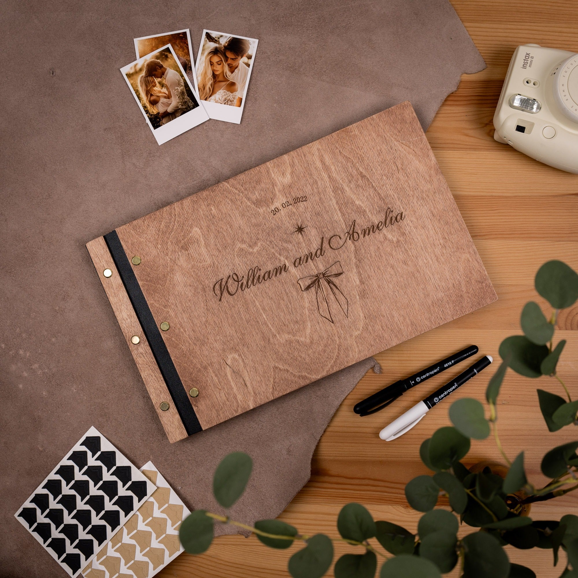 Personalized photo album with engraved names on a wooden surface with photos and stationery items.
