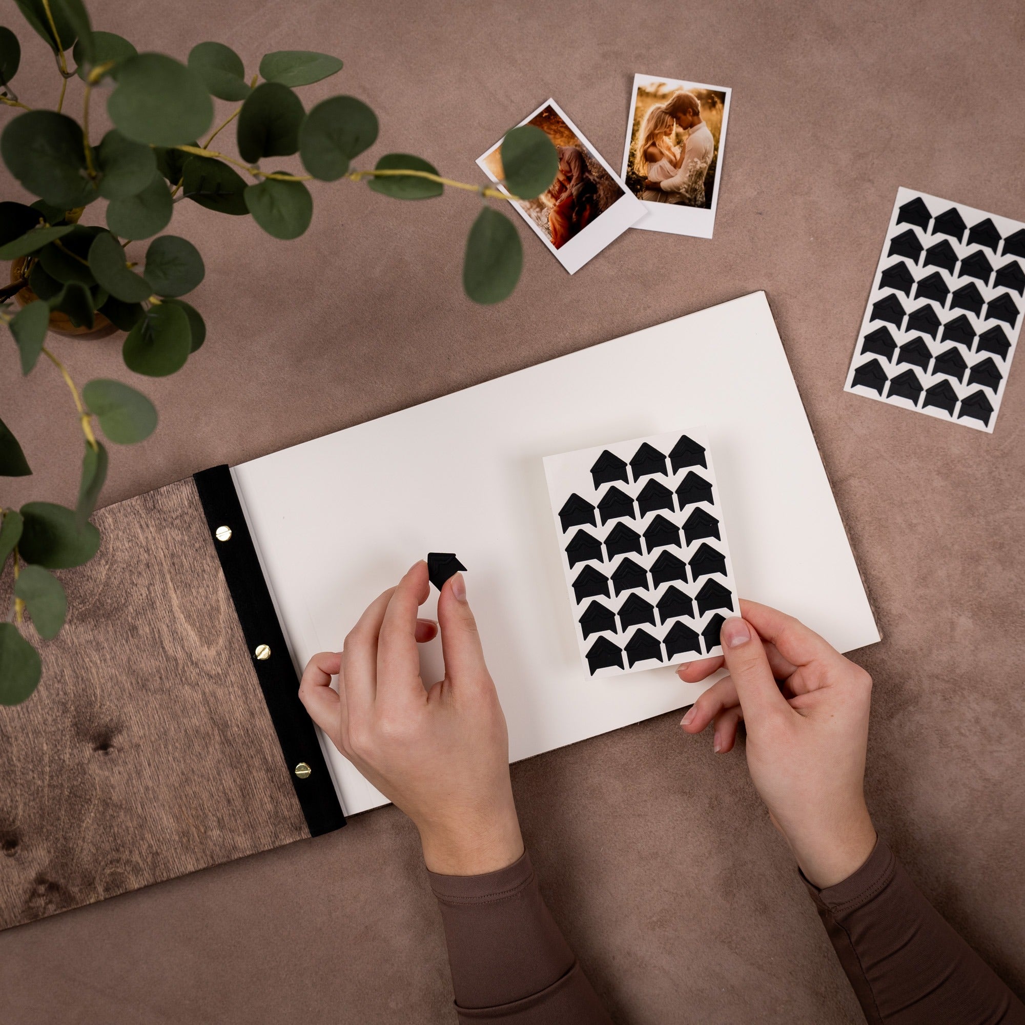 Person holding a sheet of black and white patterned paper on a brown surface with a plant and photos in the background.