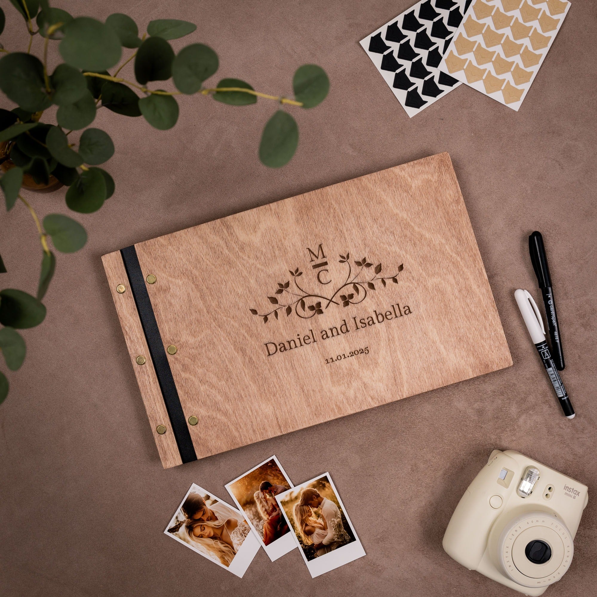 Personalized photo album with engraved names and dates on a brown surface with photos and a camera.