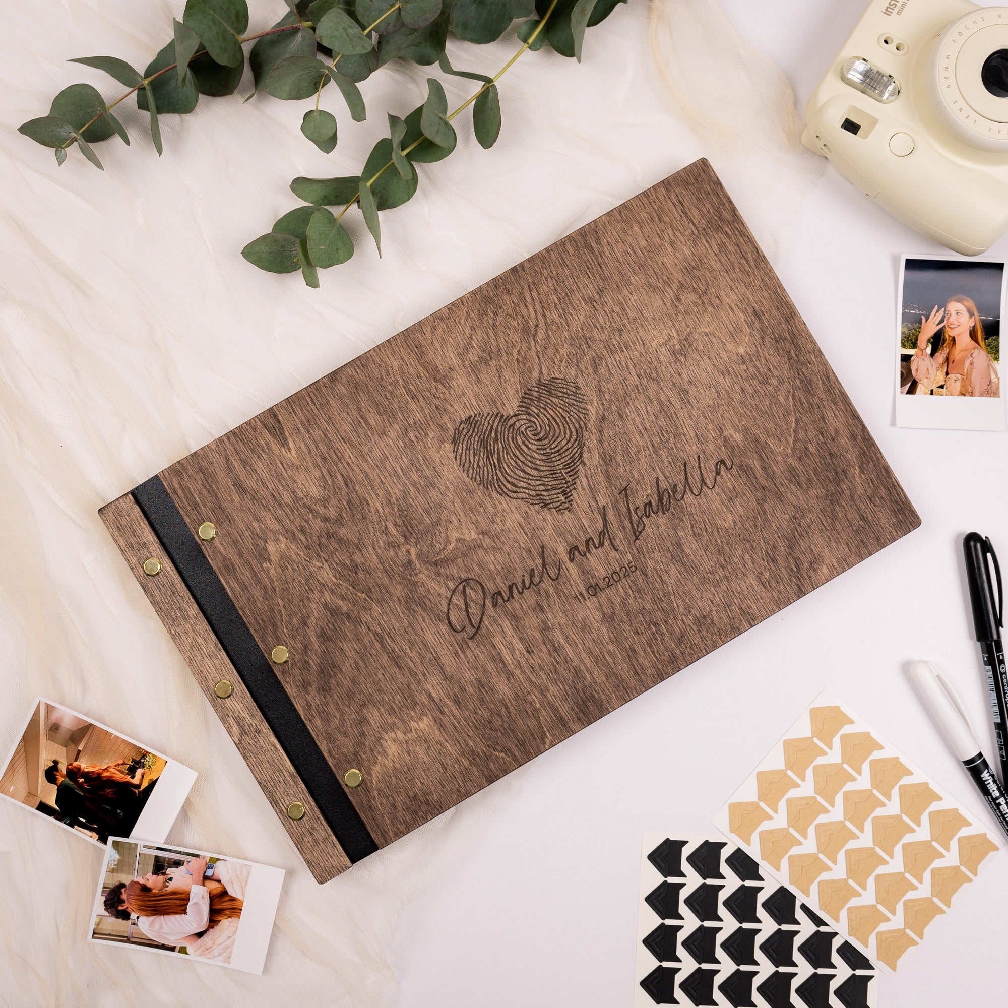 Wooden photo album with fingerprint design and text on a white surface with photos and stationery items.