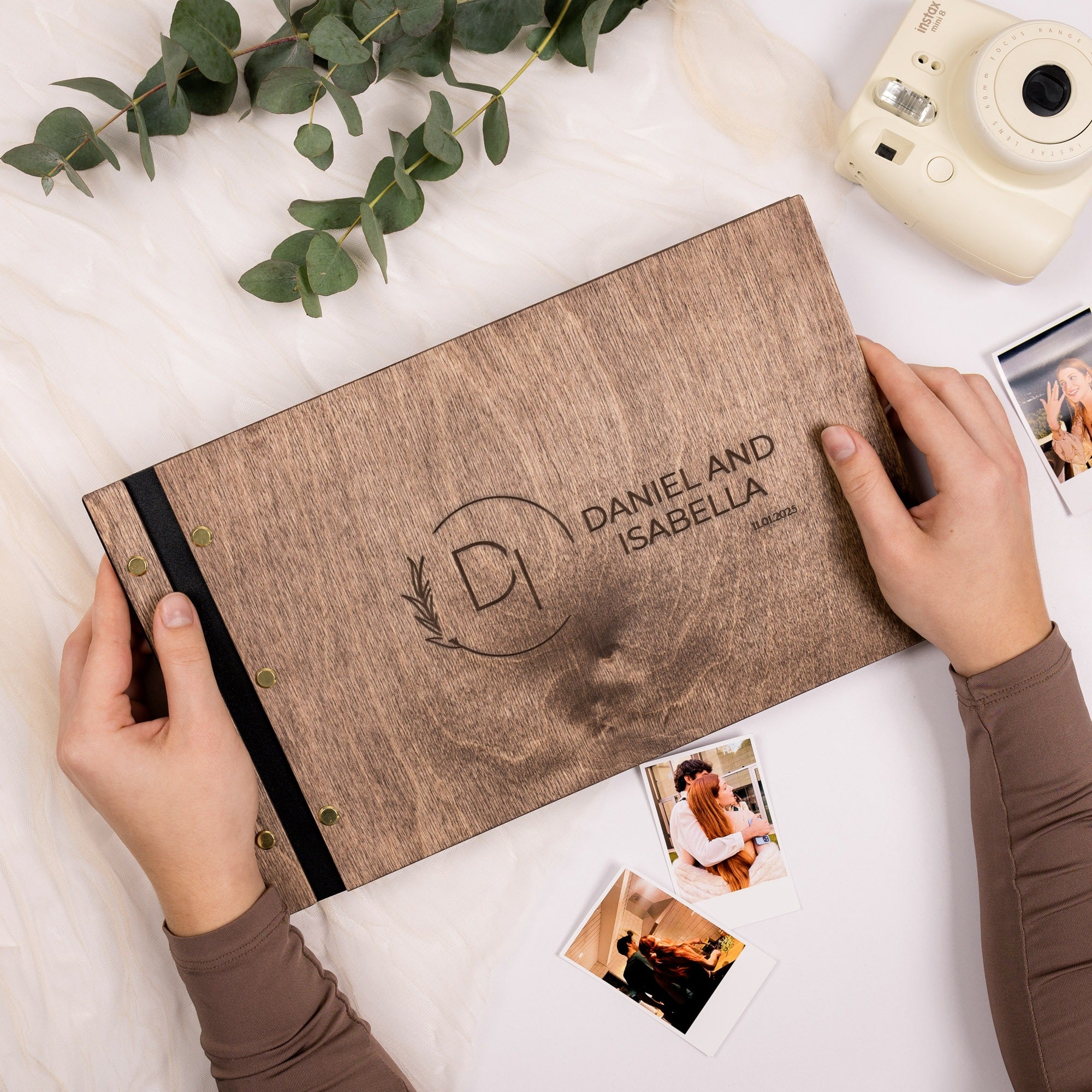 Personalized photo album with engraved name and logo on a white surface with photos and greenery.