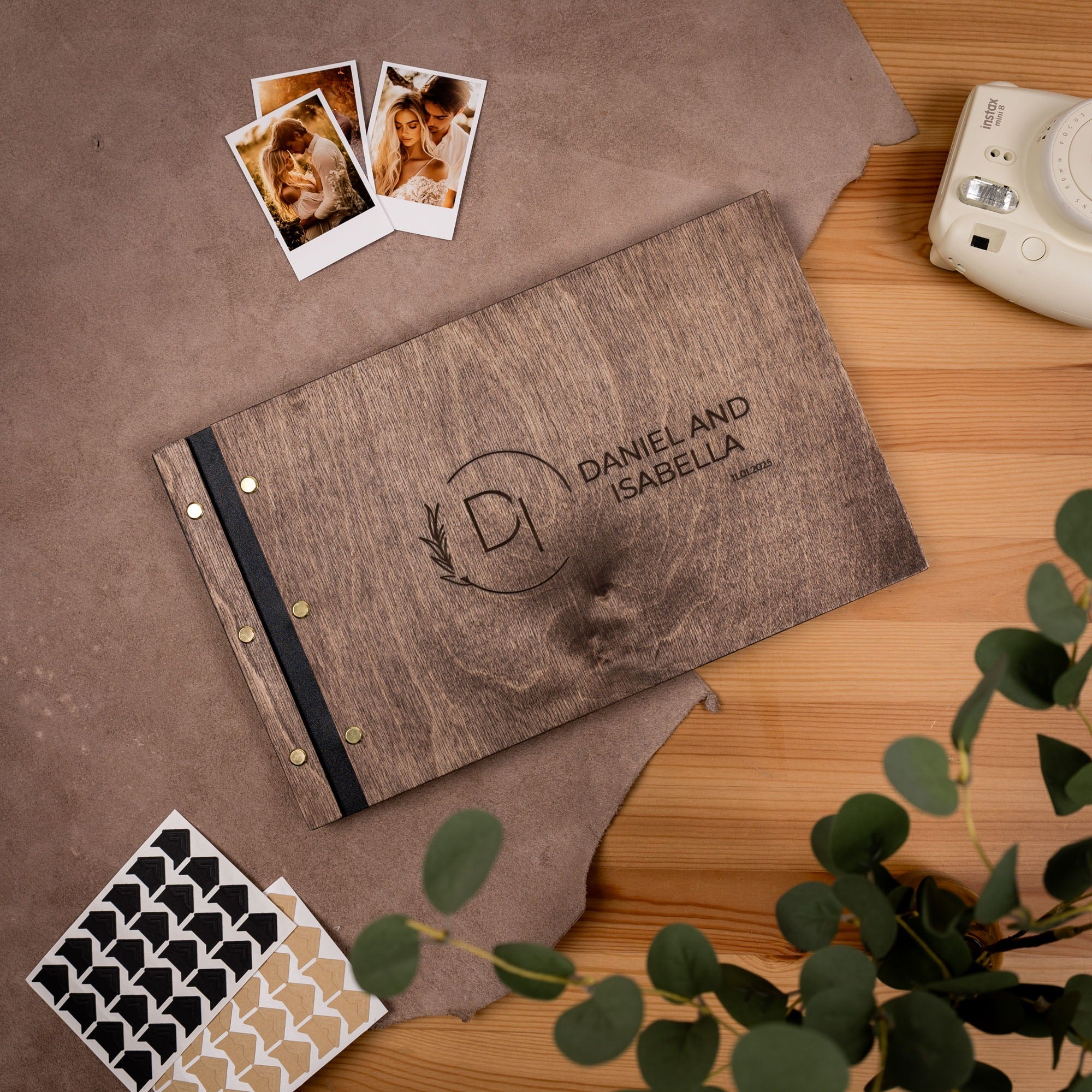 Brown photo album with 'Daniel and Isabella' on a wooden surface with photos and a camera.