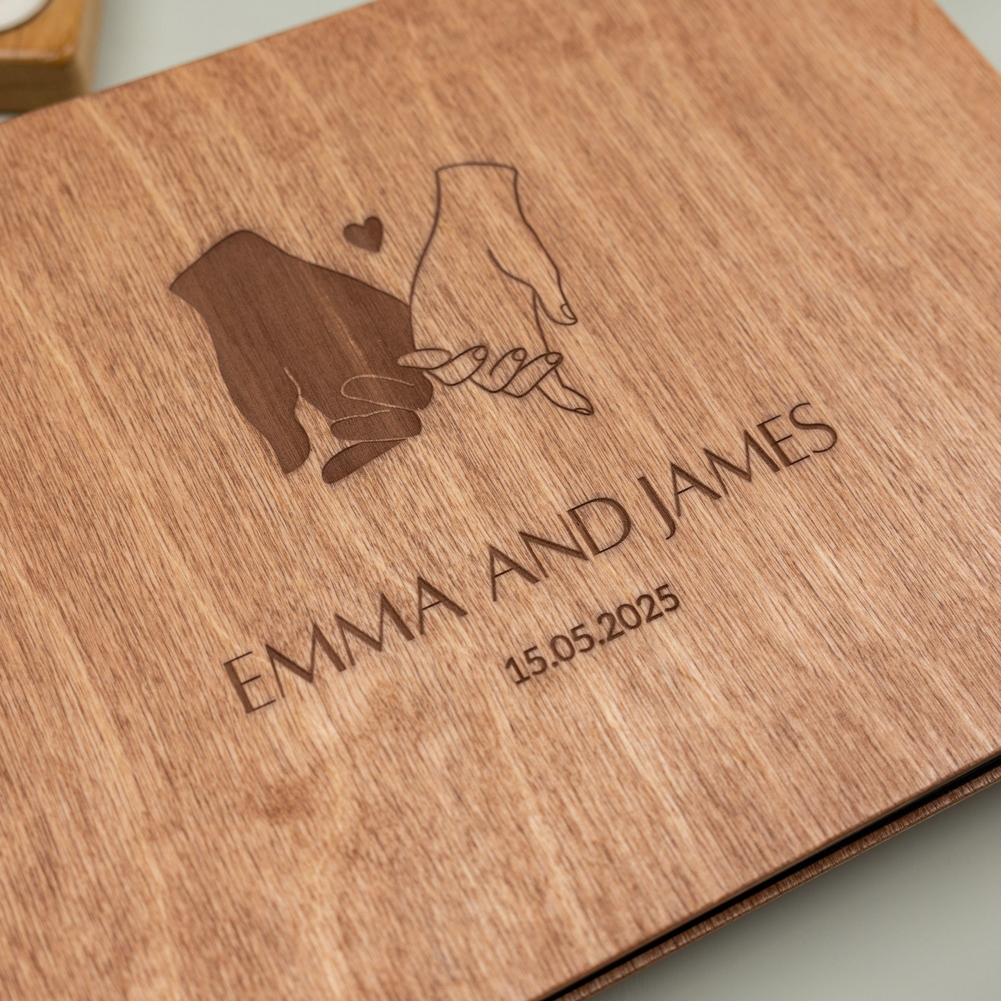 Wooden plaque with engraved design of two hands holding a heart and text 'Emma and James 15.05.2023'.