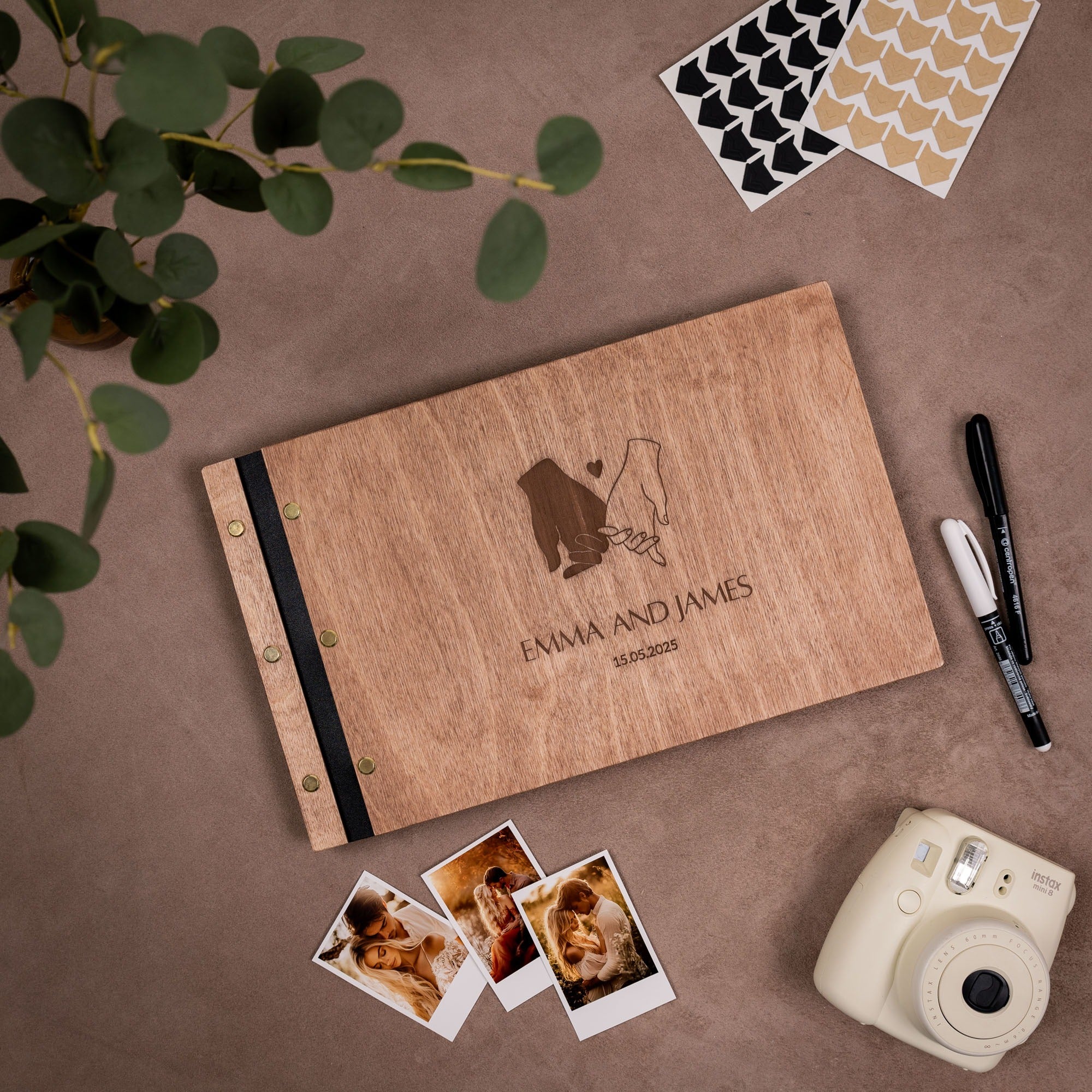 Personalized wooden photo album with engraved couple's name, photos, and a camera on a brown surface.