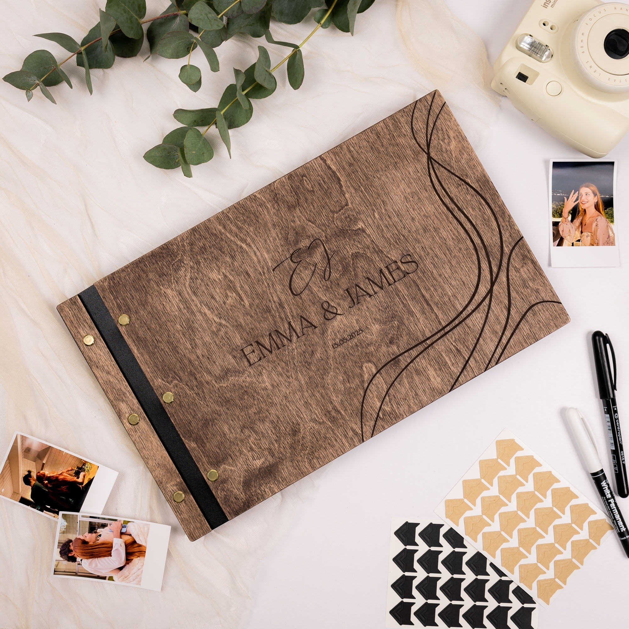 Wooden photo album with 'Emma & James' engraving on a white surface with photos and stationery.