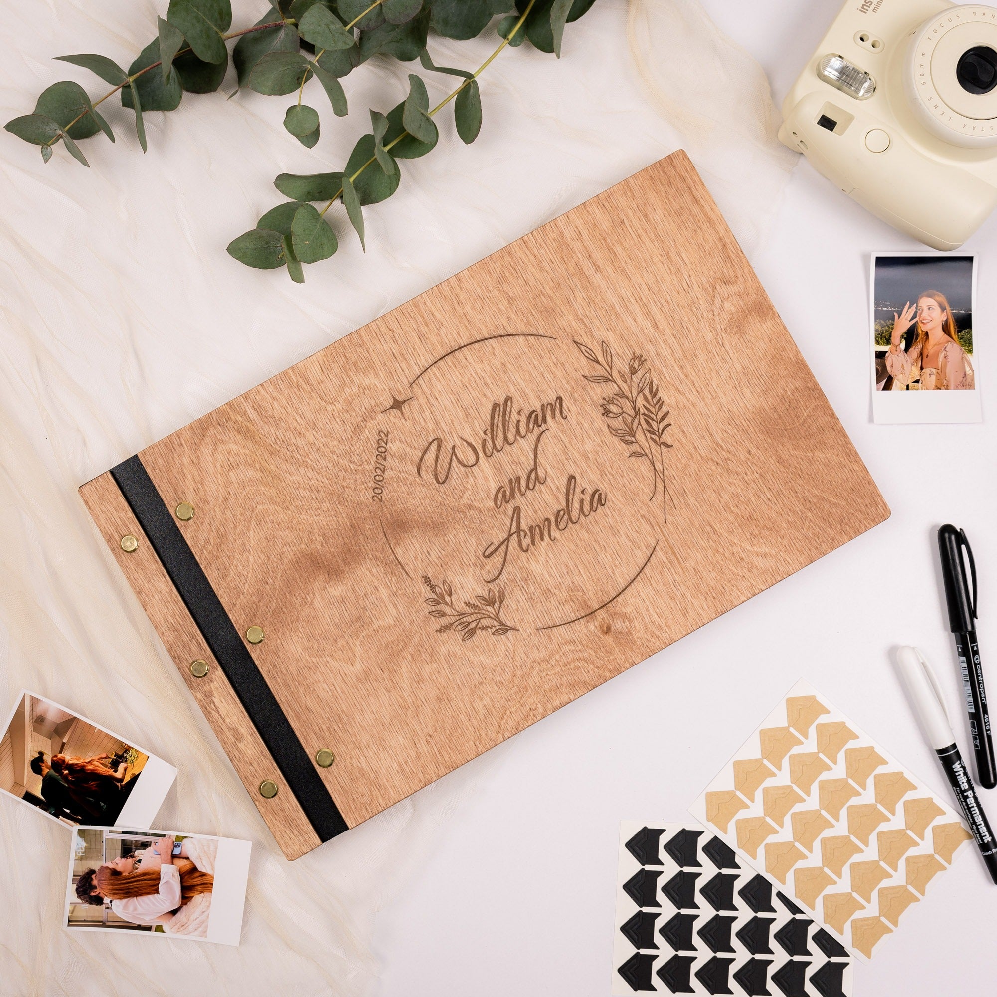 Personalized photo album with engraved names on a white surface with photos and stationery items.