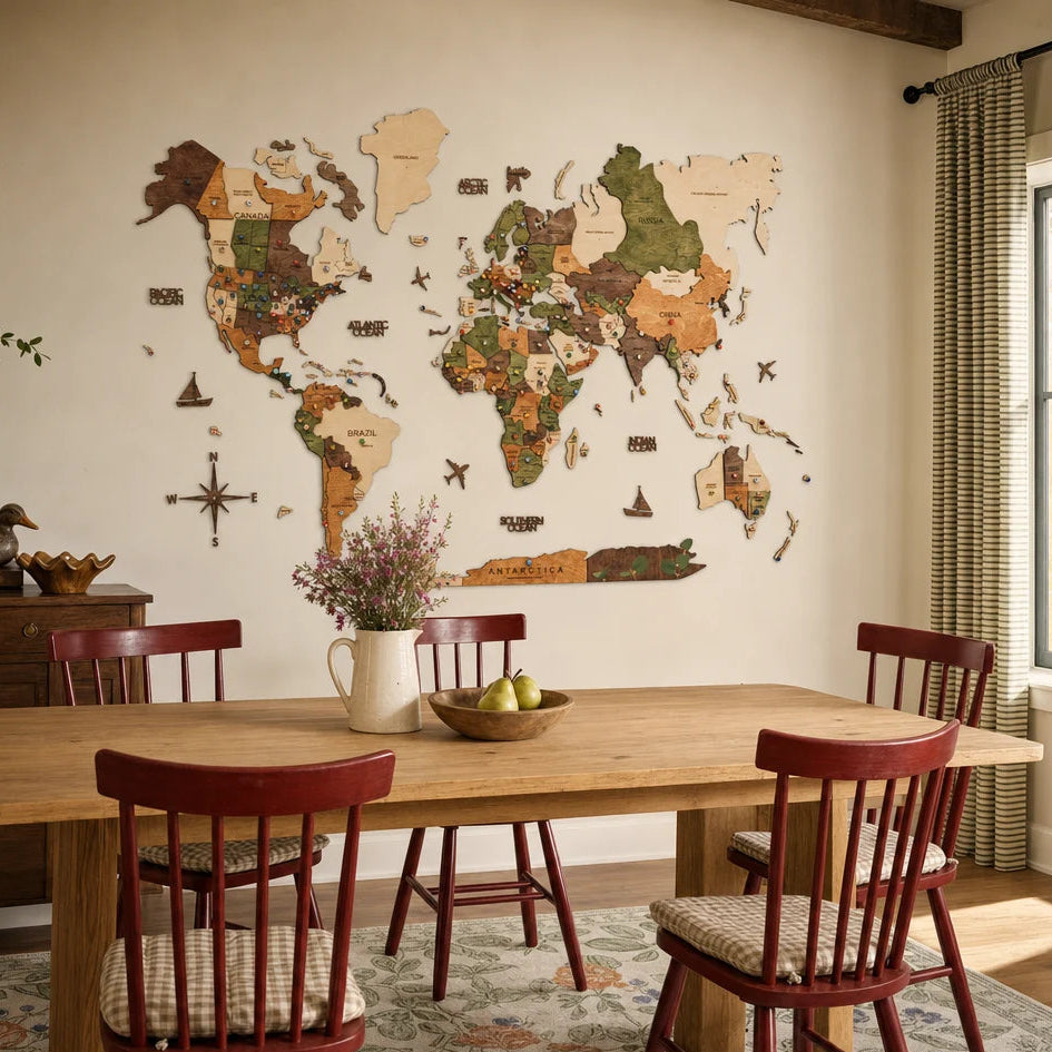 A 3D wooden world map with various wood tones and engraved country names is mounted on a white wall in a cozy dining area. Below the map, a long wooden table with a white pitcher of flowers is surrounded by four classic wooden chairs with red backrests and checkered cushions.