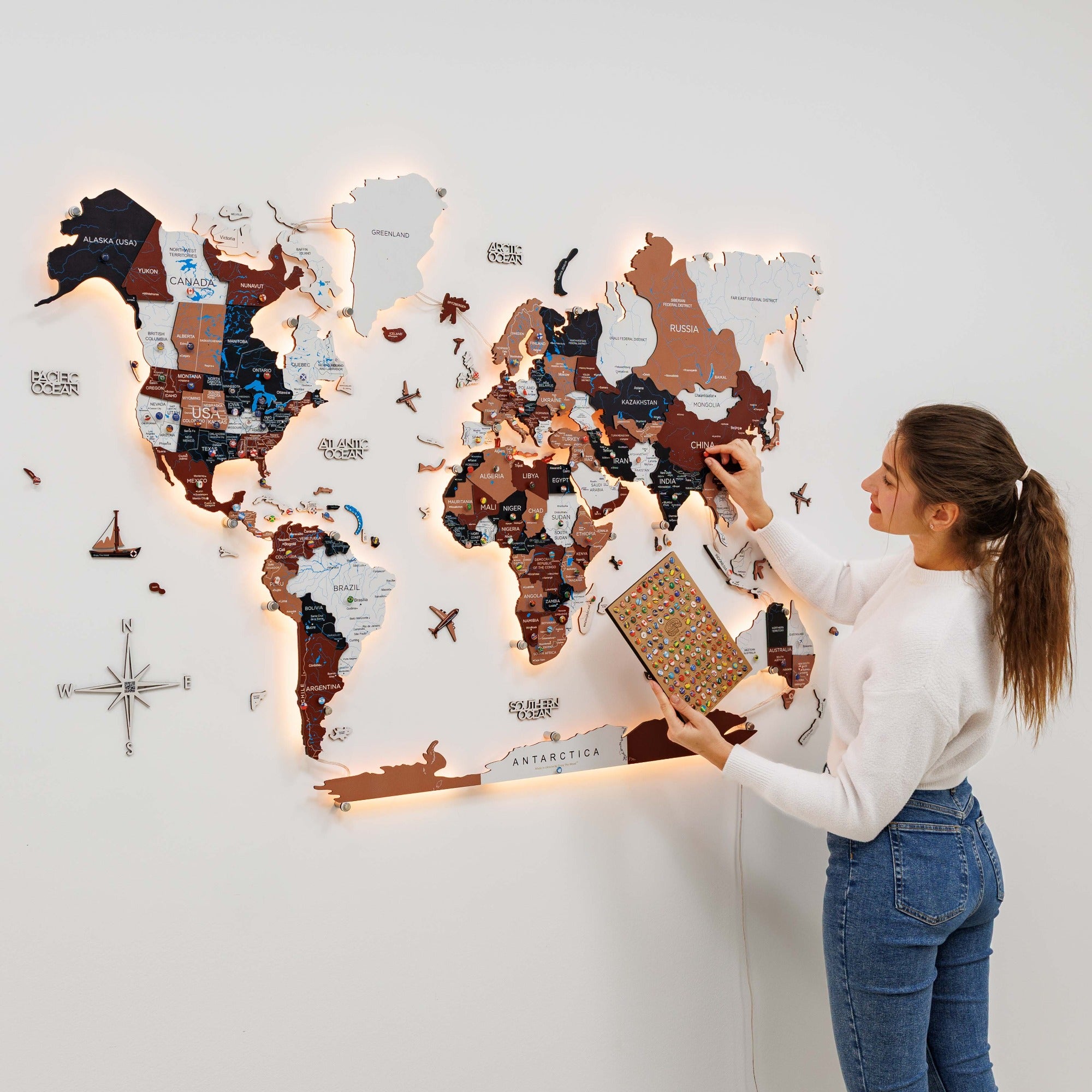 Woman interacting with a world map on a wall, holding a travel journal.
