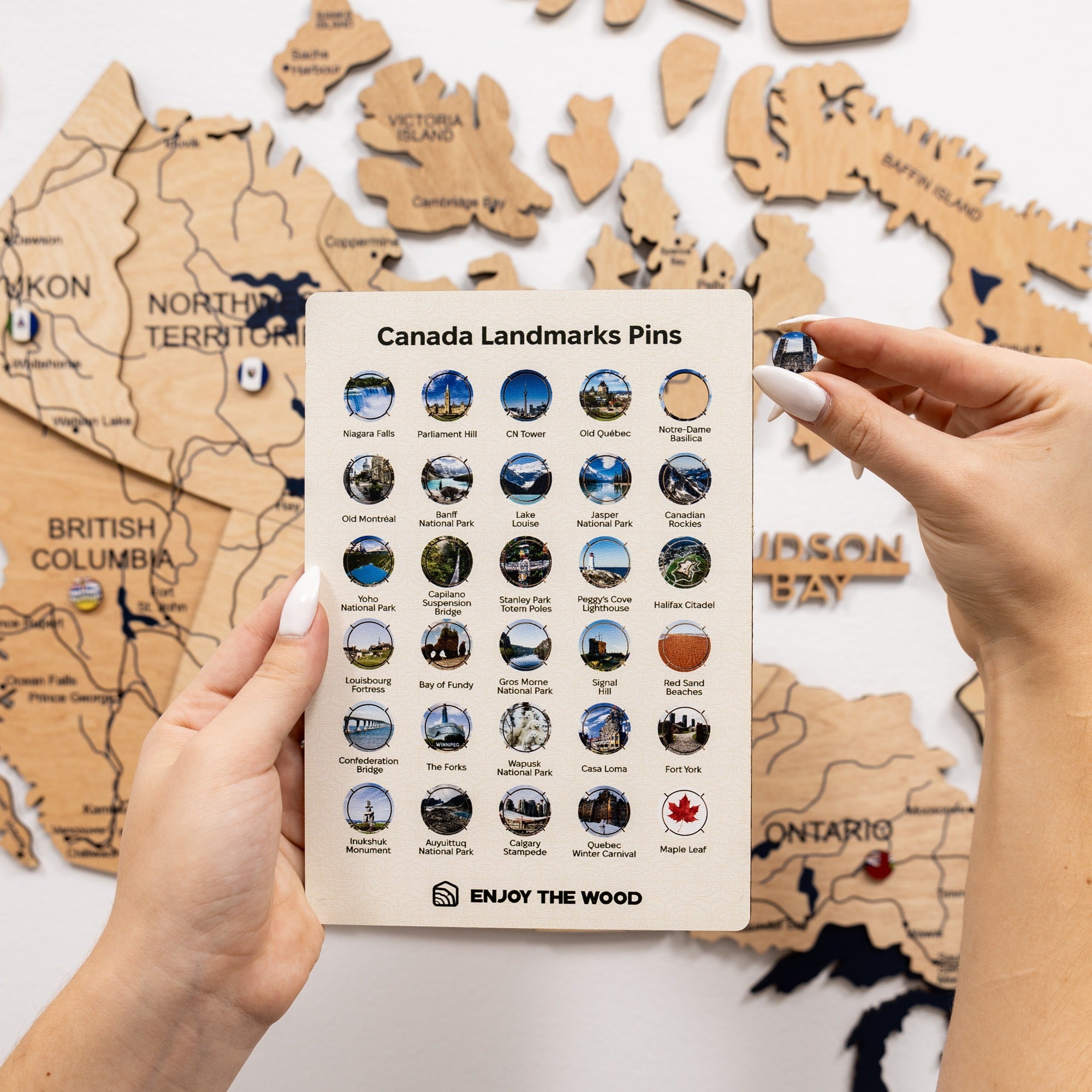 Card with Canada landmarks pins held over a wooden map of Canada.